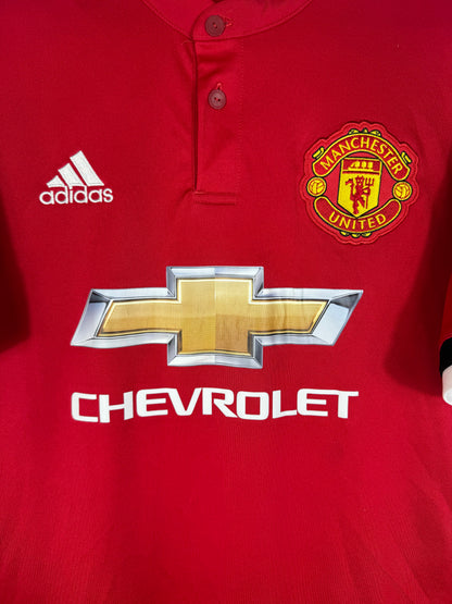 Gros plan sur l'écusson de Manchester United brodé et le détail du col à deux boutons.