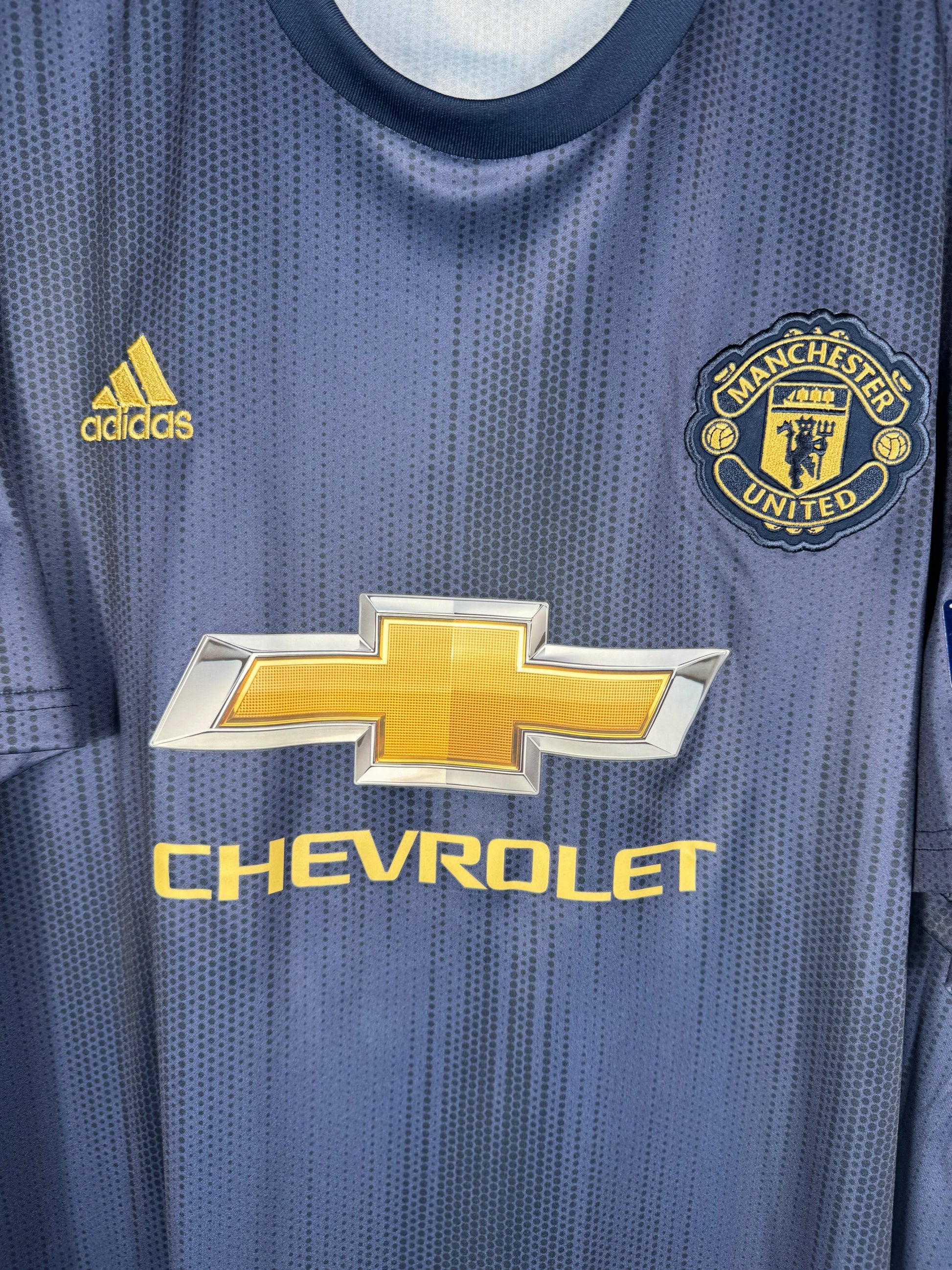 Gros plan sur l'écusson thermocollé de Manchester United et le logo adidas or.