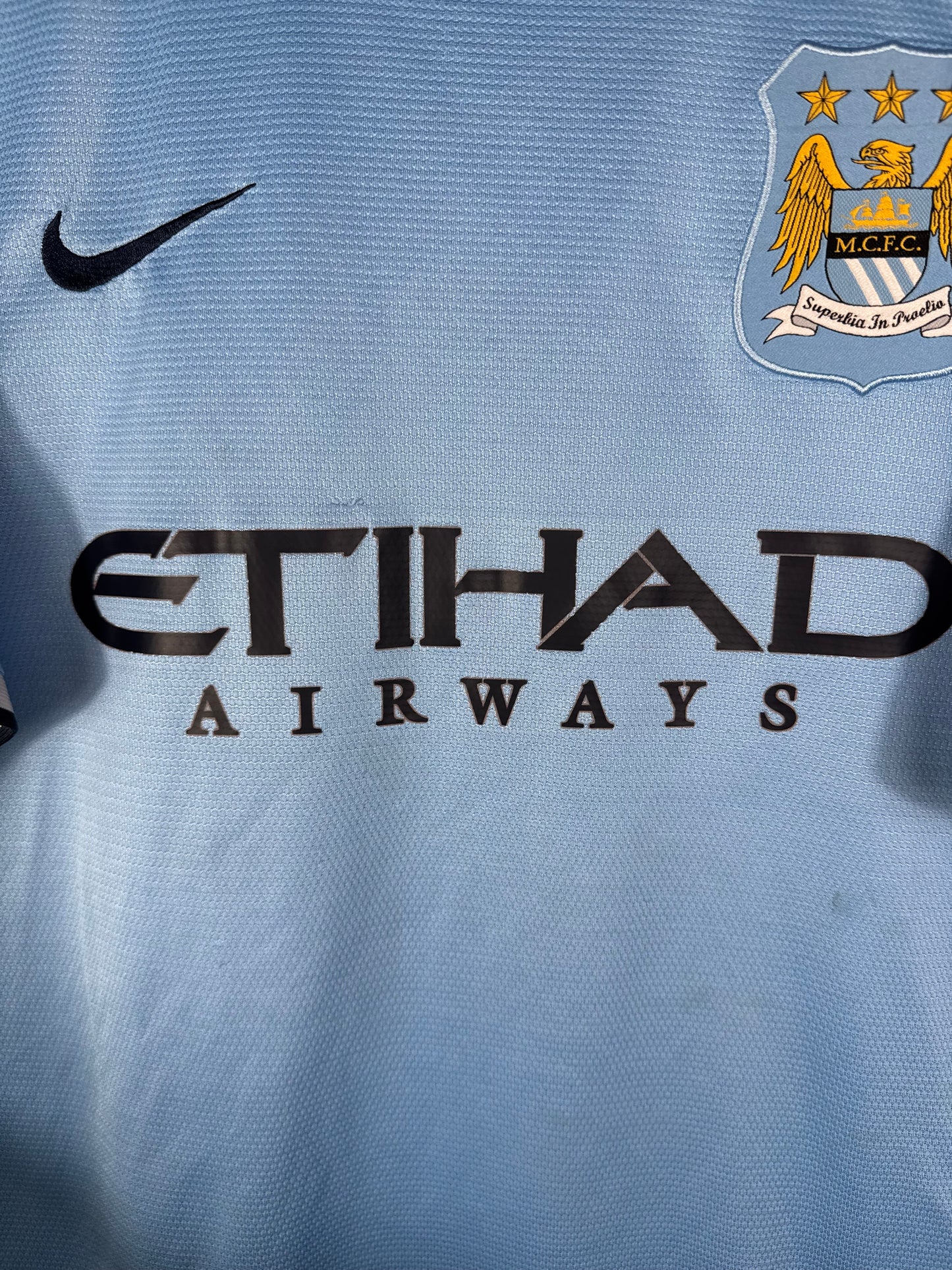 Gros plan sur l'ancien écusson de Manchester City, le logo Nike bleu marine et le sponsor Etihad sur le maillot domicile.