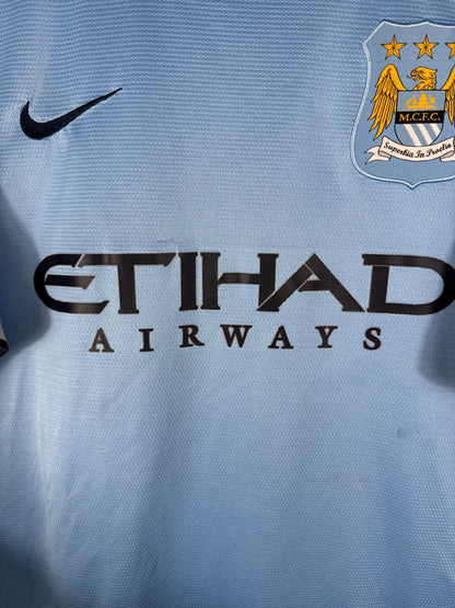 Gros plan sur l'ancien écusson de Manchester City, le logo Nike bleu marine et le sponsor Etihad sur le maillot domicile.