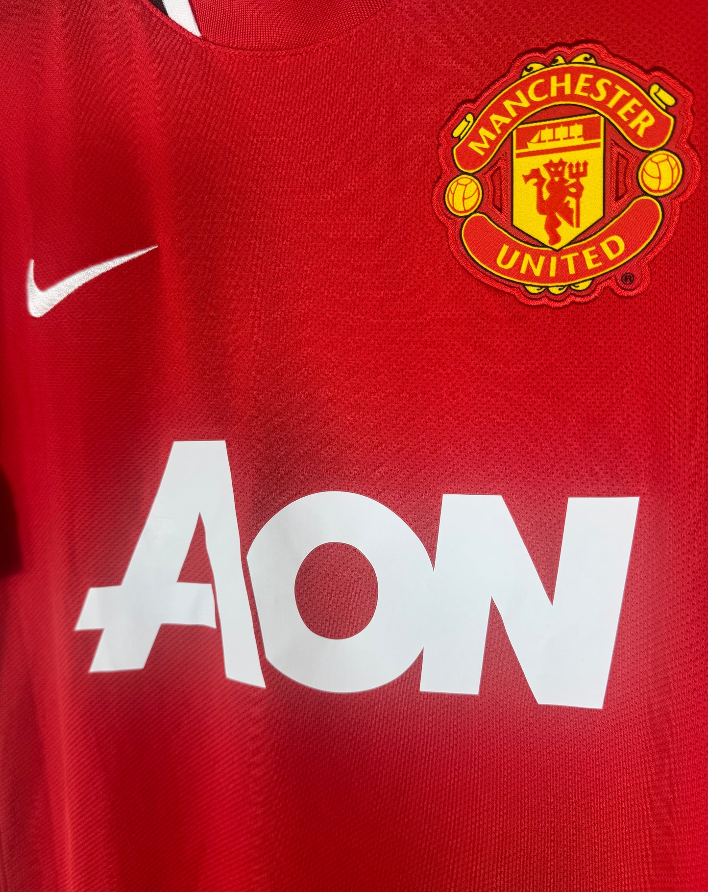 Gros plan sur l'écusson Manchester United, le swoosh Nike et le sponsor Aon.
