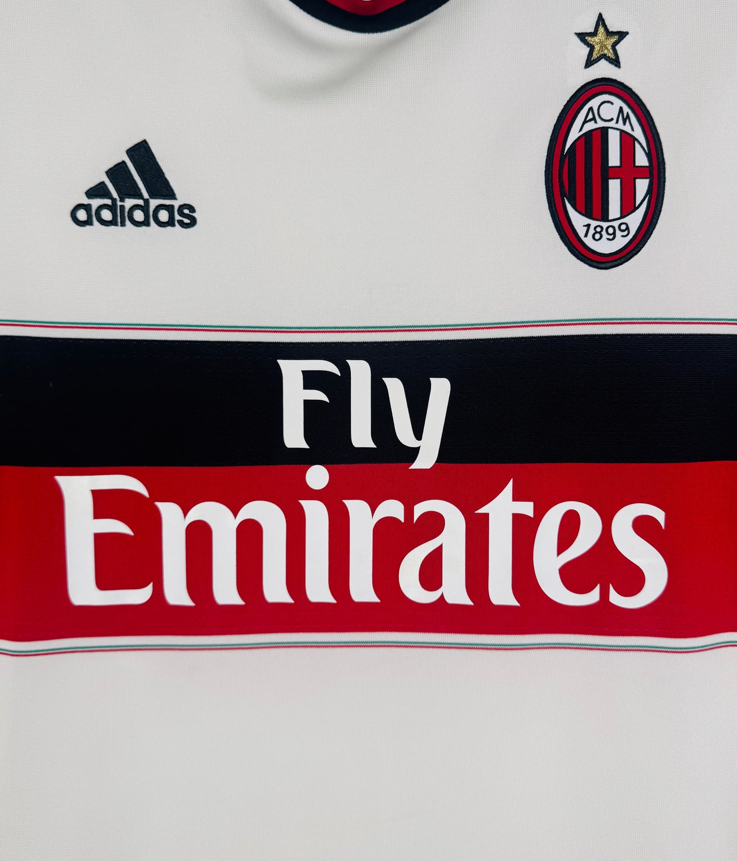 Gros plan sur l'écusson AC Milan brodé et le sponsor Fly Emirates sur la bande poitrine.