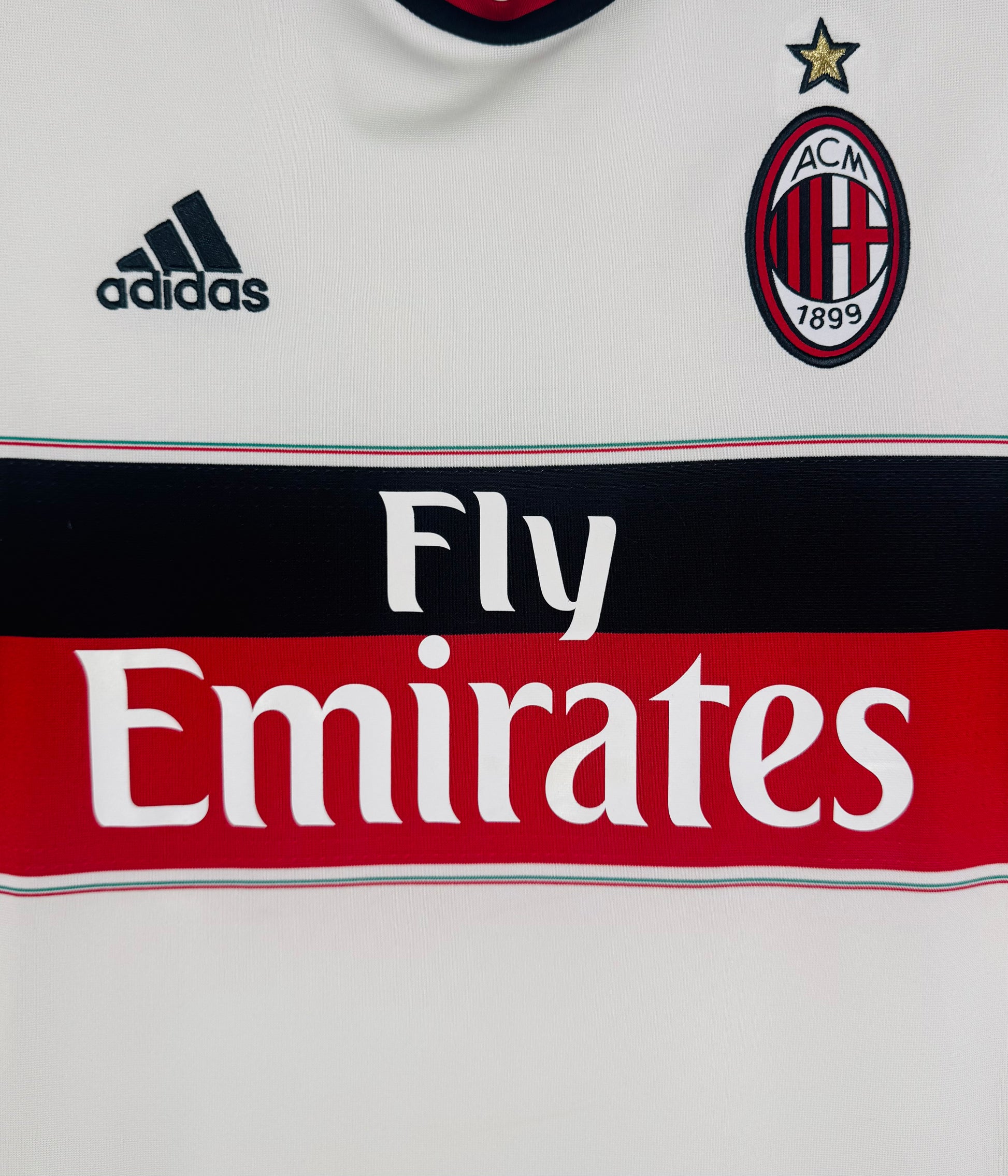 Gros plan sur l'écusson AC Milan brodé et le sponsor Fly Emirates sur la bande poitrine.