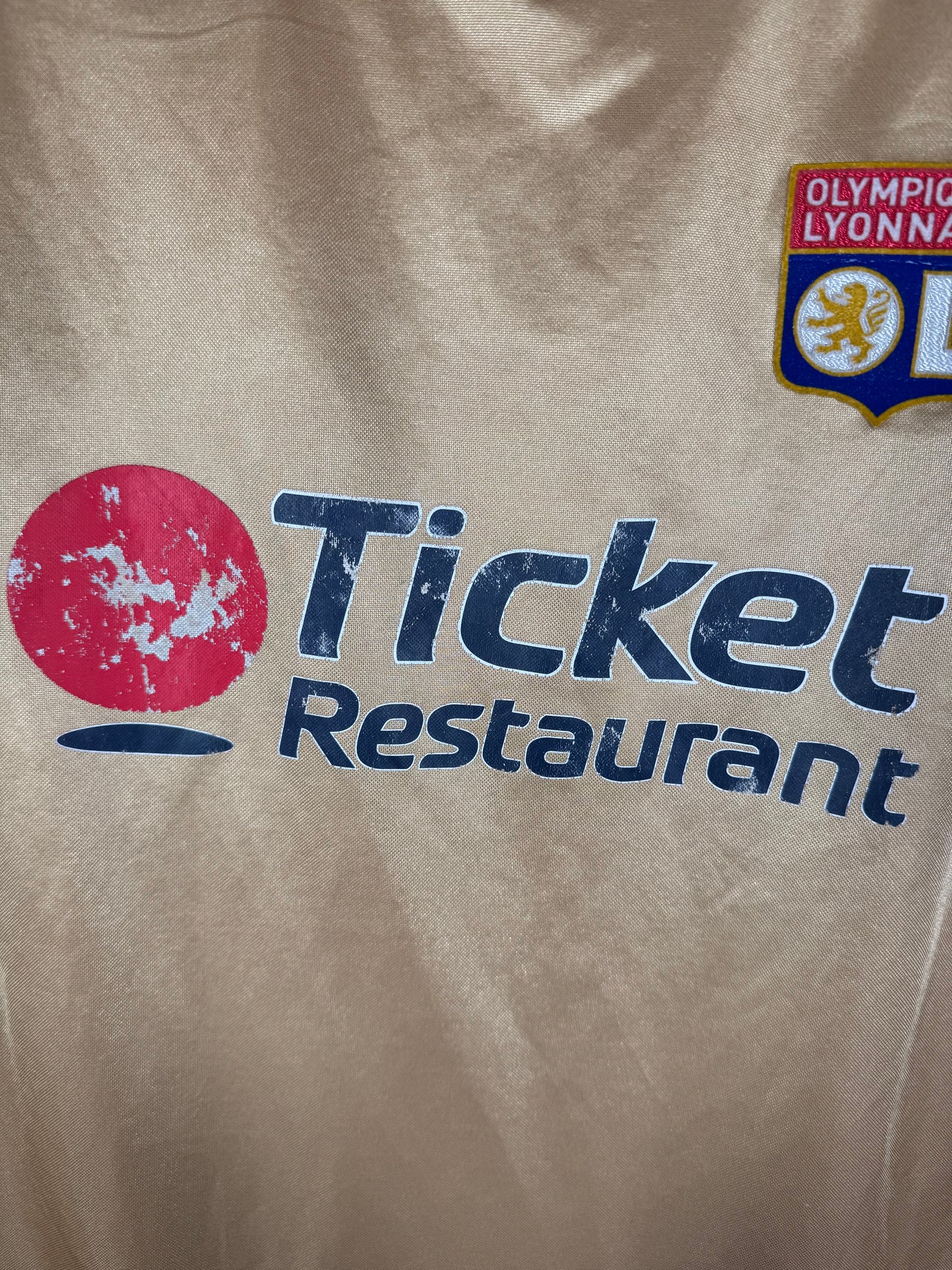 Gros plan sur l'écusson central de l'Olympique Lyonnais et le logo Umbro brodé.