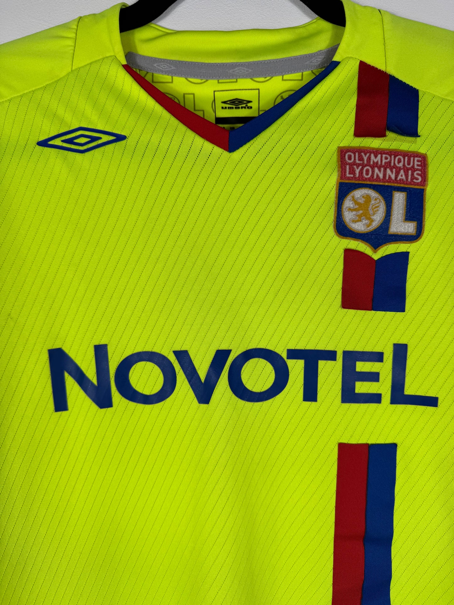 Gros plan sur l'écusson de l'OL et le logo Umbro brodé sur le tissu jaune fluorescent.