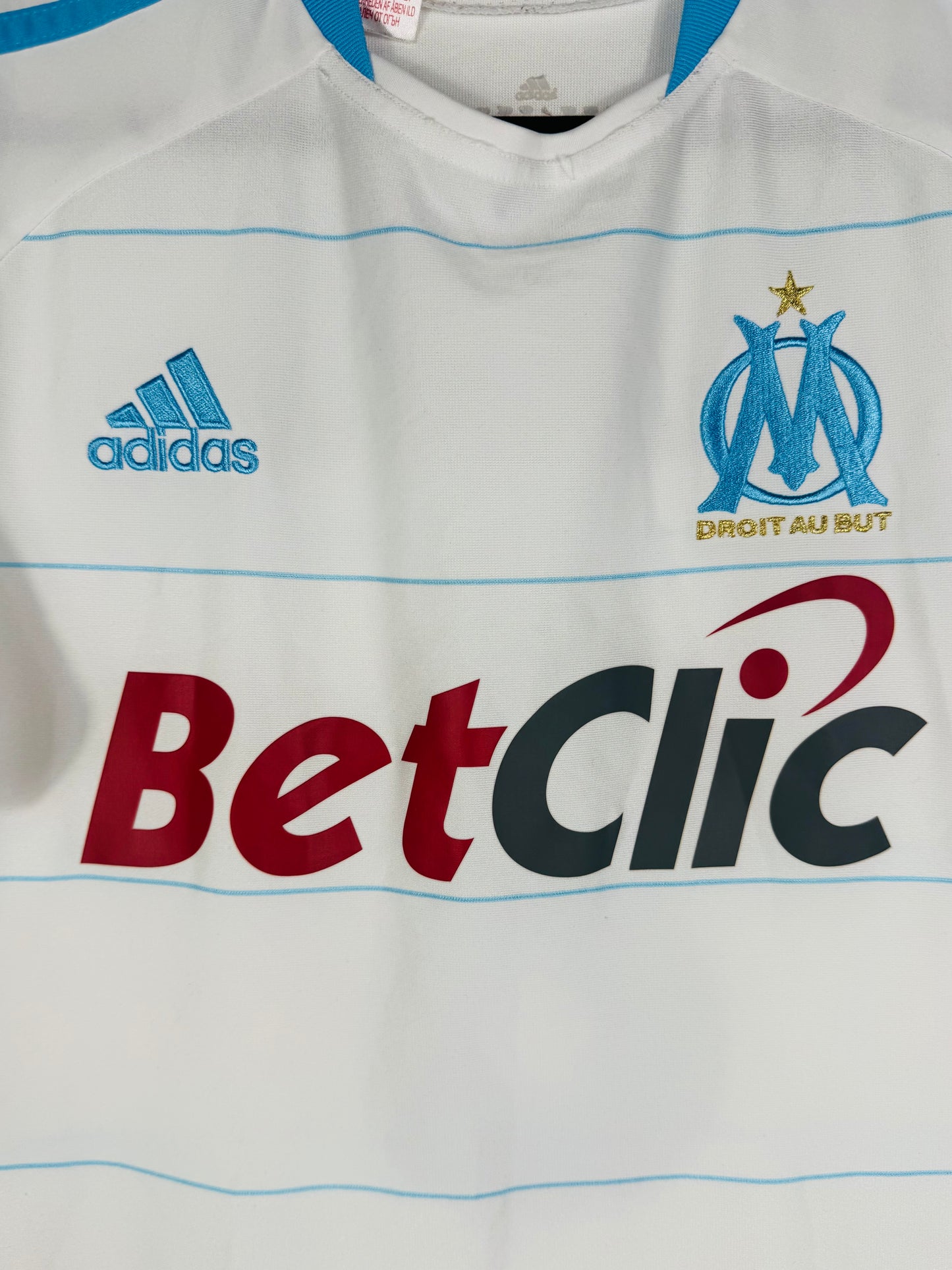 Gros plan sur l'écusson Olympique de Marseille, le logo Adidas bleu et le sponsor BetClic.