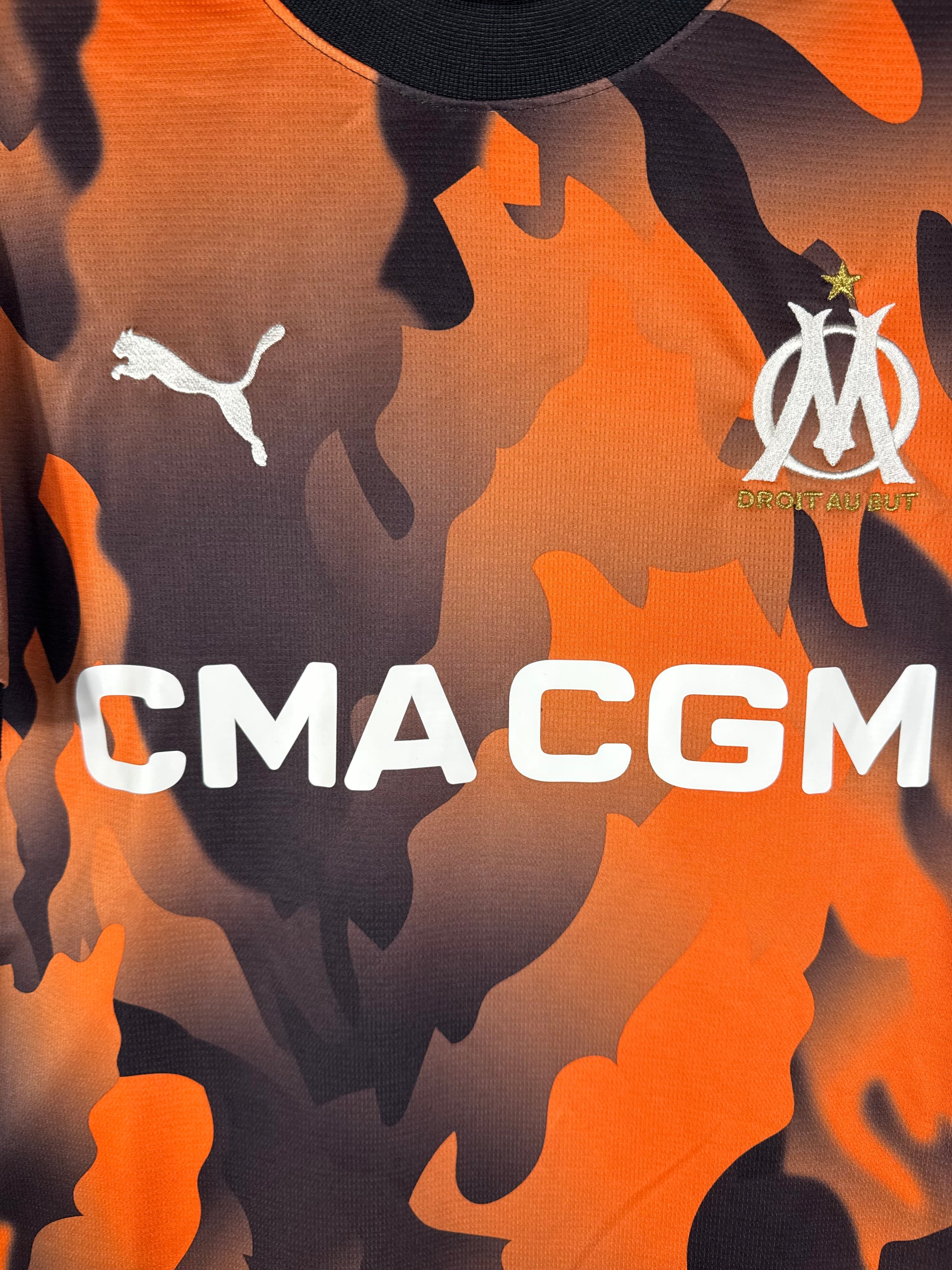 Gros plan sur l'écusson de l'OM et le logo Puma déclinés en orange et noir.