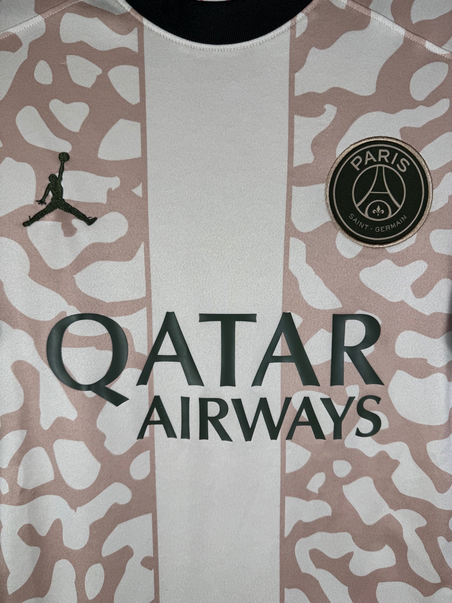 Gros plan sur l'écusson du Paris Saint-Germain et le logo Jumpman bleu marine sur le tissu beige.