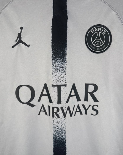 Gros plan sur le logo Jordan noir et l'écusson du Paris Saint-Germain sur maillot gris.