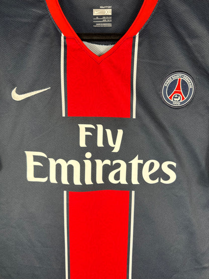 Gros plan sur l'écusson du Paris Saint-Germain et le logo Nike blanc sur la bande rouge du maillot domicile.