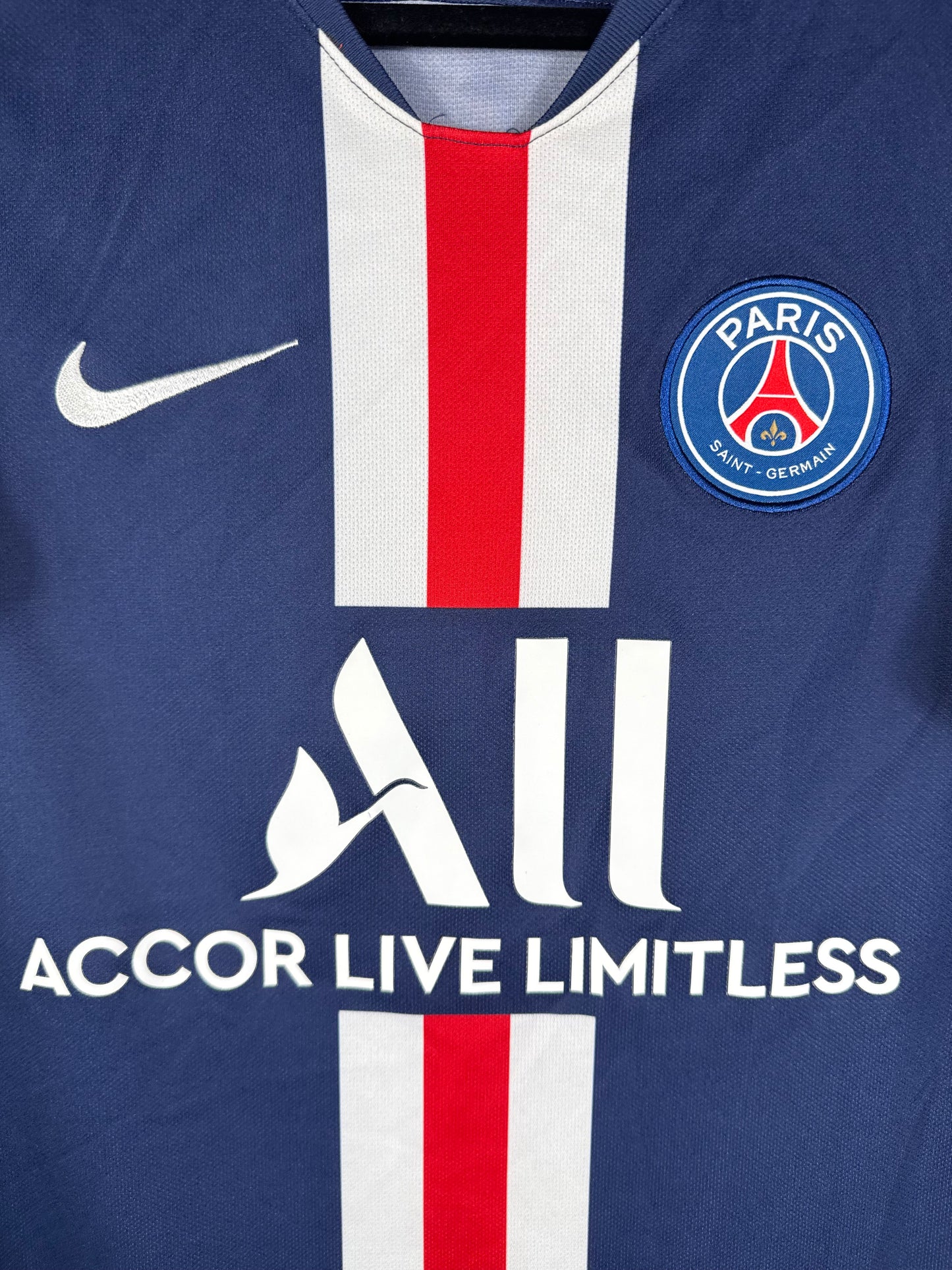 Gros plan sur l'écusson du Paris Saint-Germain et le logo Nike brodés sur les bandes blanches et rouges.