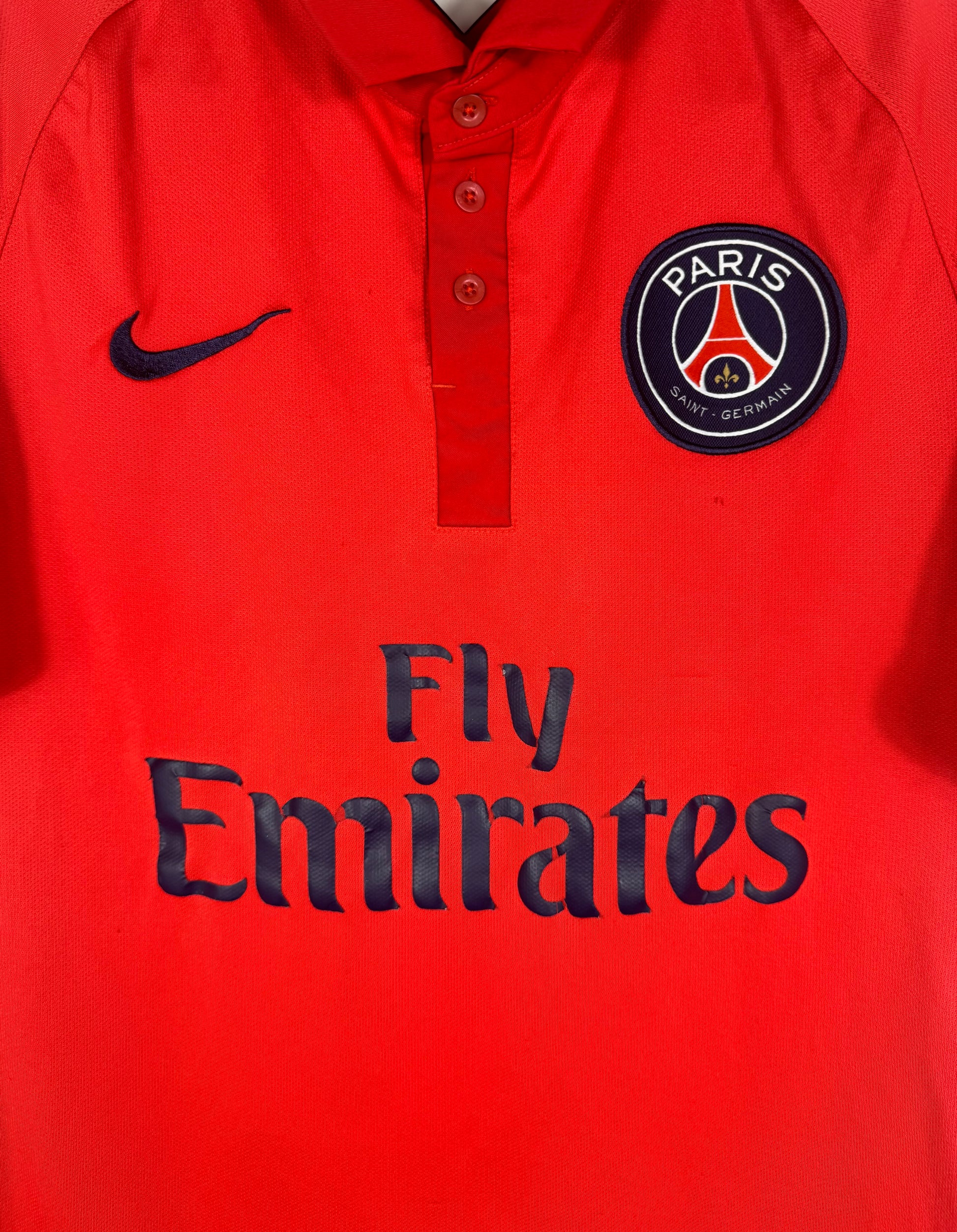 Gros plan sur l'écusson Paris Saint-Germain et le sponsor Fly Emirates sur fond rouge.