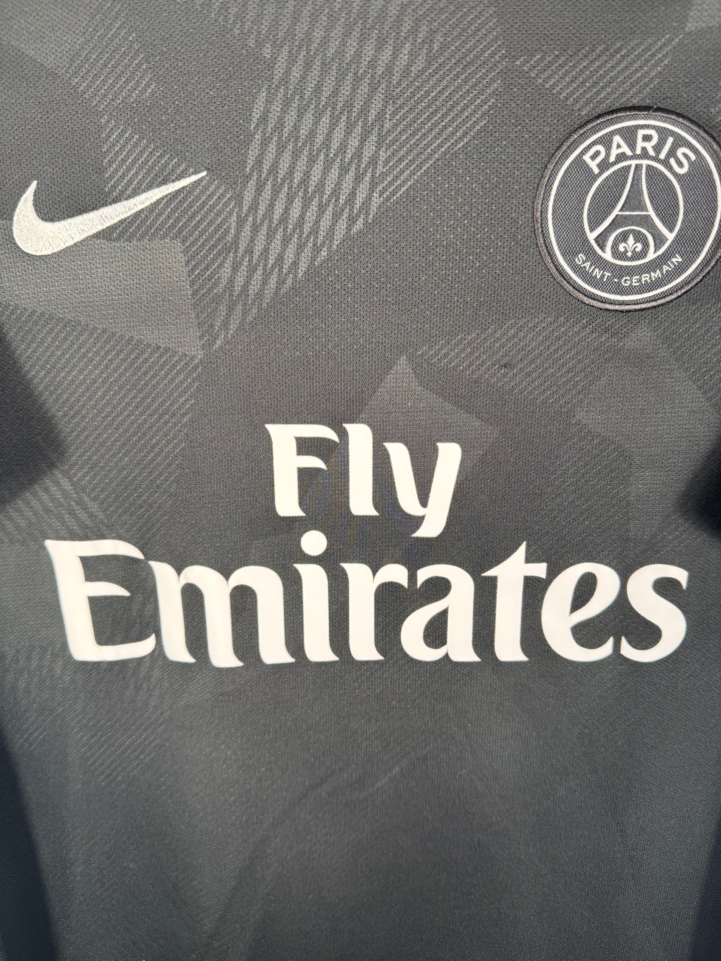 Gros plan sur l'écusson du PSG et le logo Nike argentés sur le tissu technique camouflage.