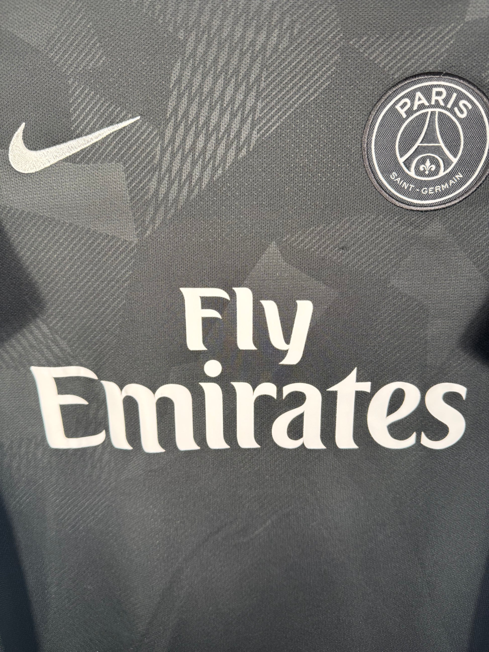 Gros plan sur l'écusson du PSG et le logo Nike argentés sur le tissu technique camouflage.