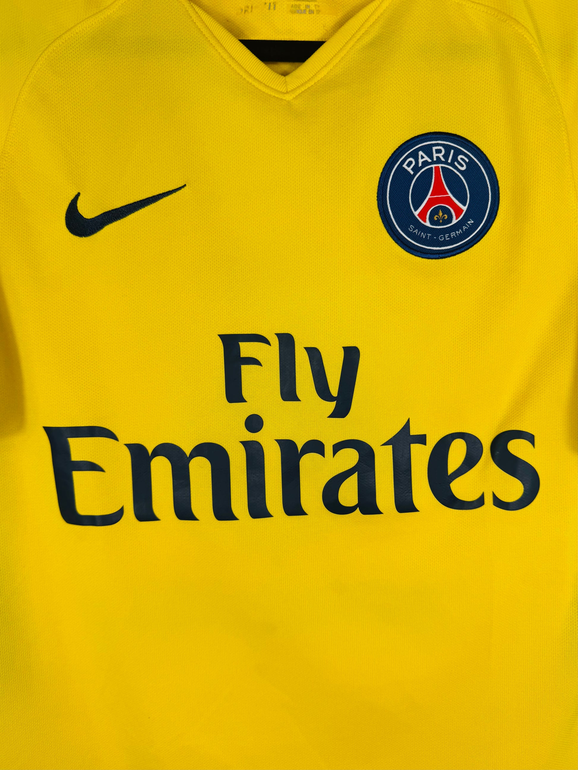 Gros plan sur l'écusson du Paris Saint-Germain et le swoosh Nike sur le tissu jaune.