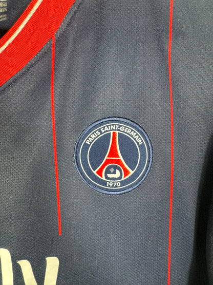 Gros plan sur l'écusson du Paris Saint-Germain brodé sur le tissu bleu à fines rayures rouges.