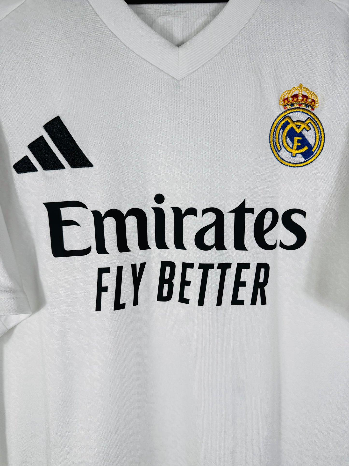 Gros plan sur l'écusson brodé du Real Madrid et le logo Adidas noir sur le tissu texturé blanc.