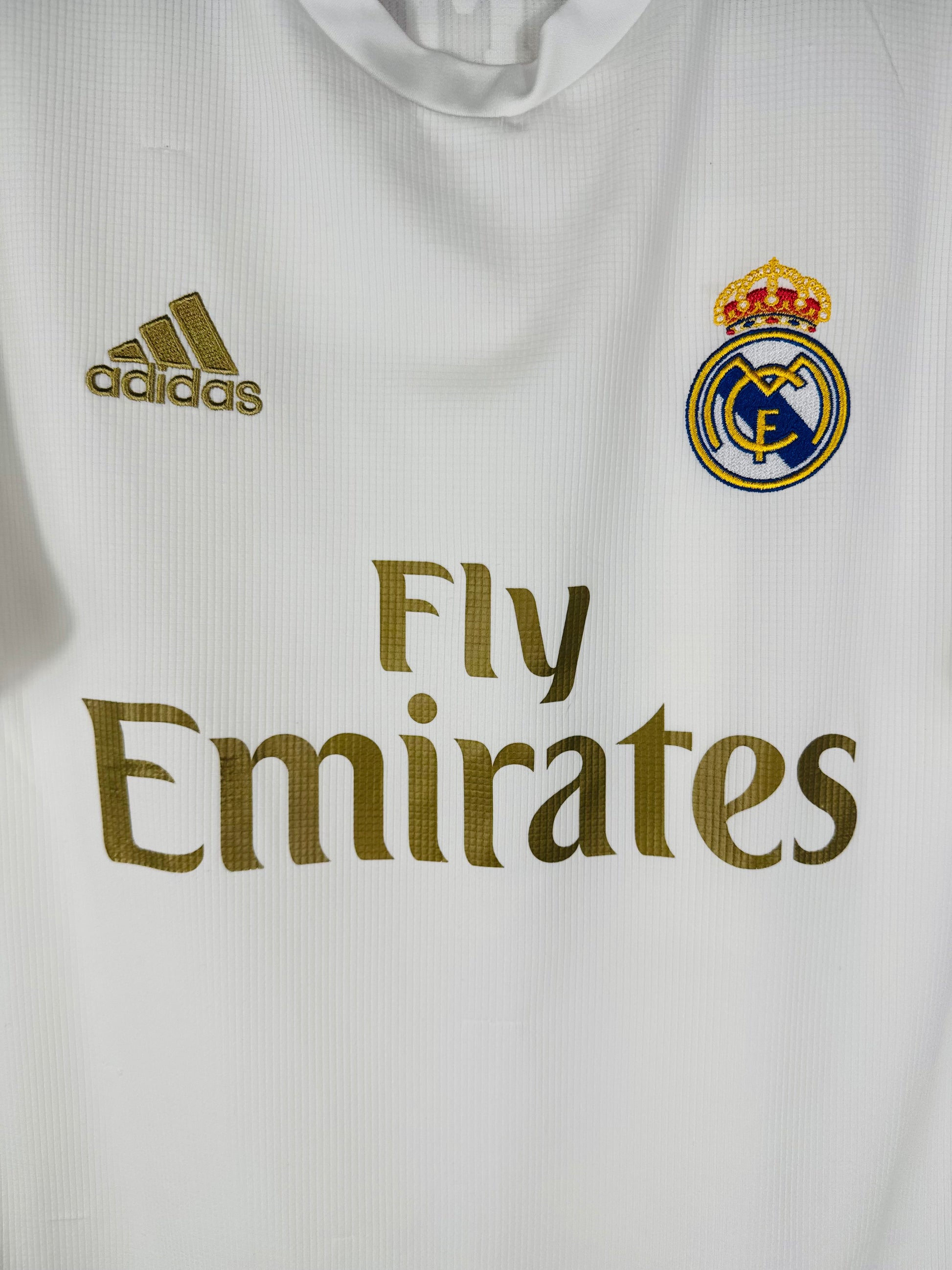 Gros plan sur l'écusson du Real Madrid et le logo Adidas brodés en or sur le maillot domicile.