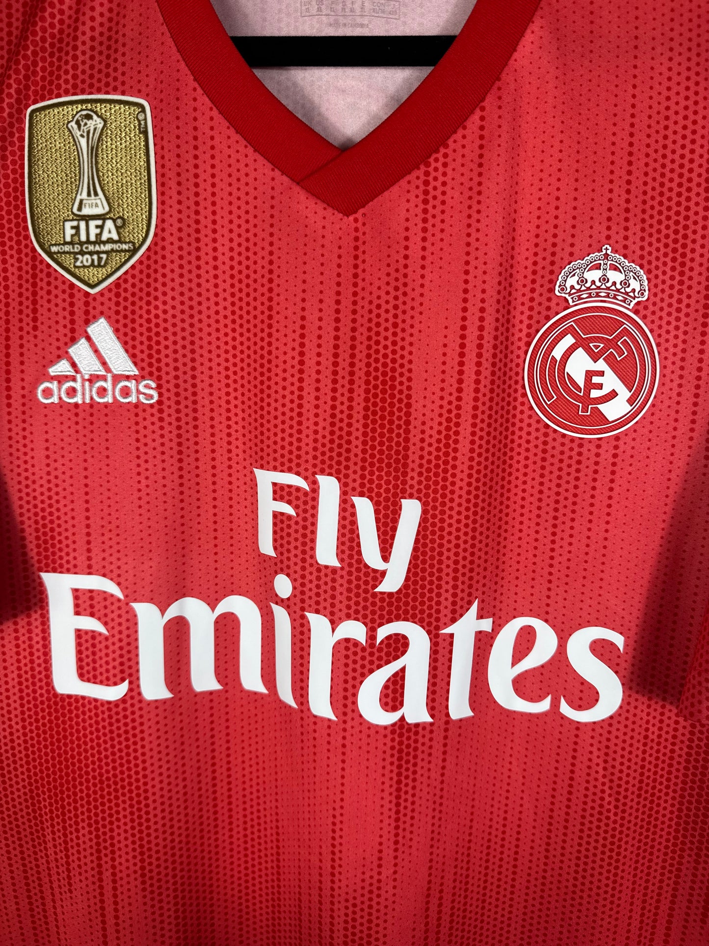 Gros plan sur l'écusson monochrome blanc du Real Madrid et le col en V du maillot recyclé.