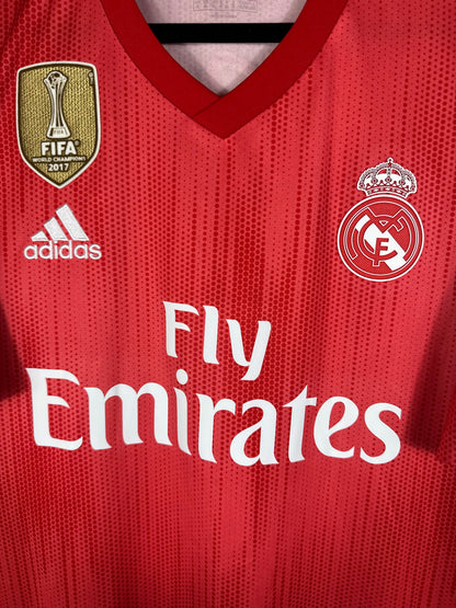 Gros plan sur l'écusson monochrome blanc du Real Madrid et le col en V du maillot recyclé.