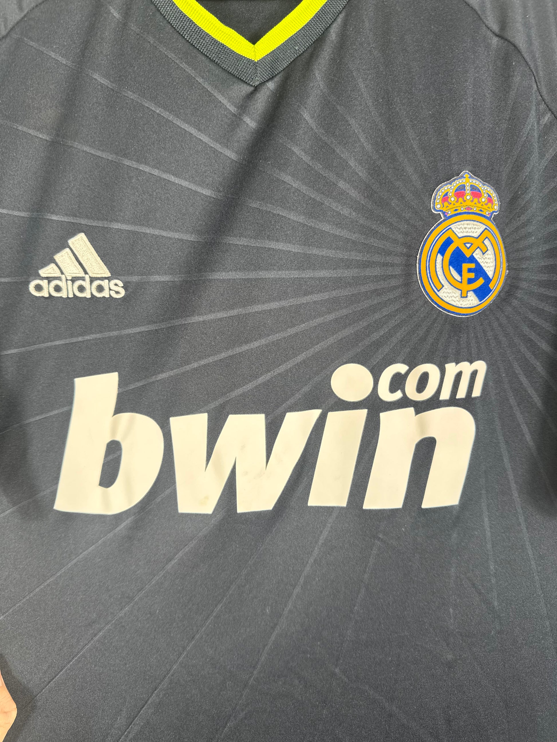 Gros plan sur l'écusson du Real Madrid, le logo Adidas et le motif rayonnant sur le tissu.