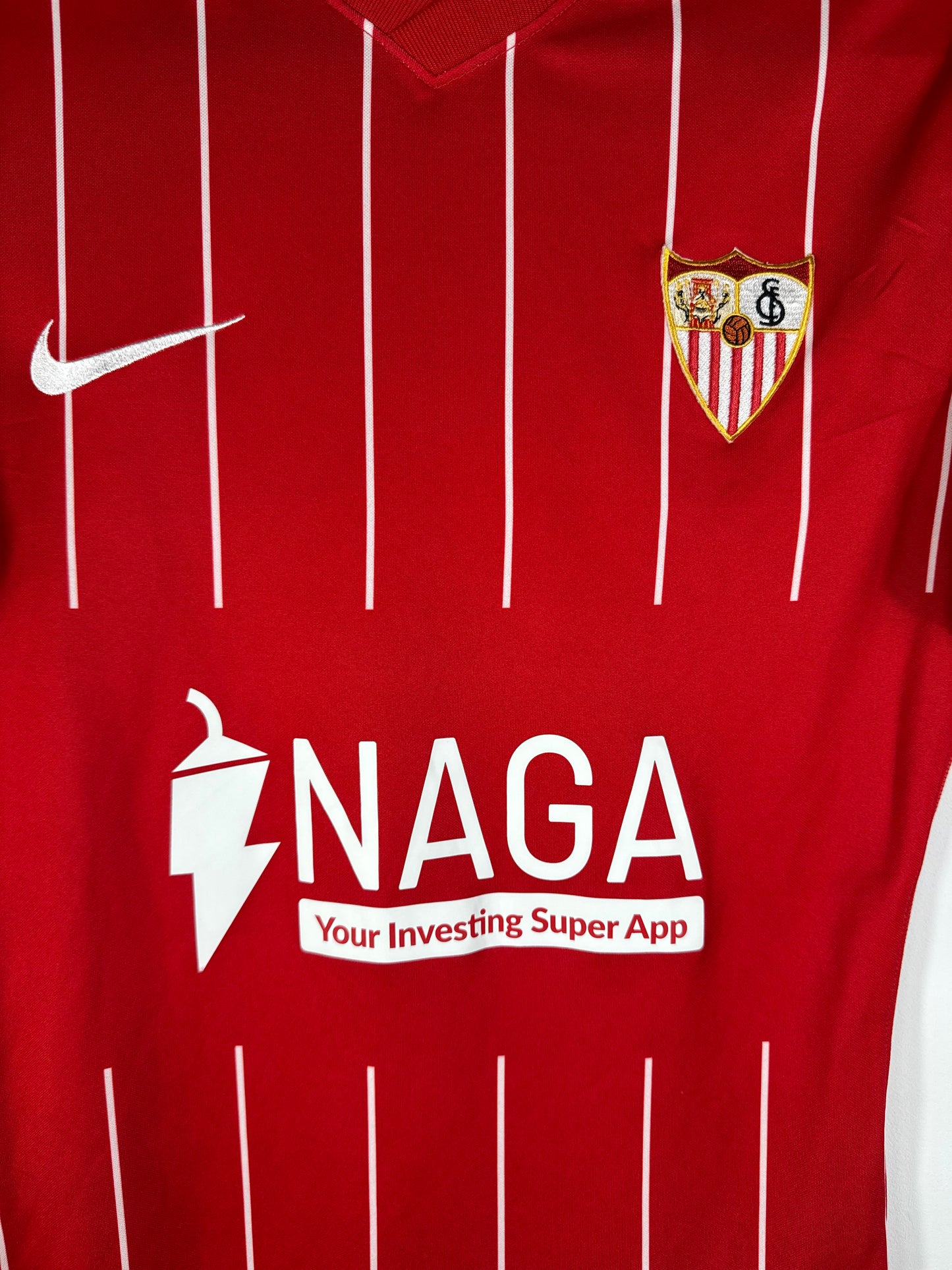 Gros plan sur l'écusson du Sevilla FC et le logo Nike blancs thermocollés sur le tissu rouge "Pro Version".