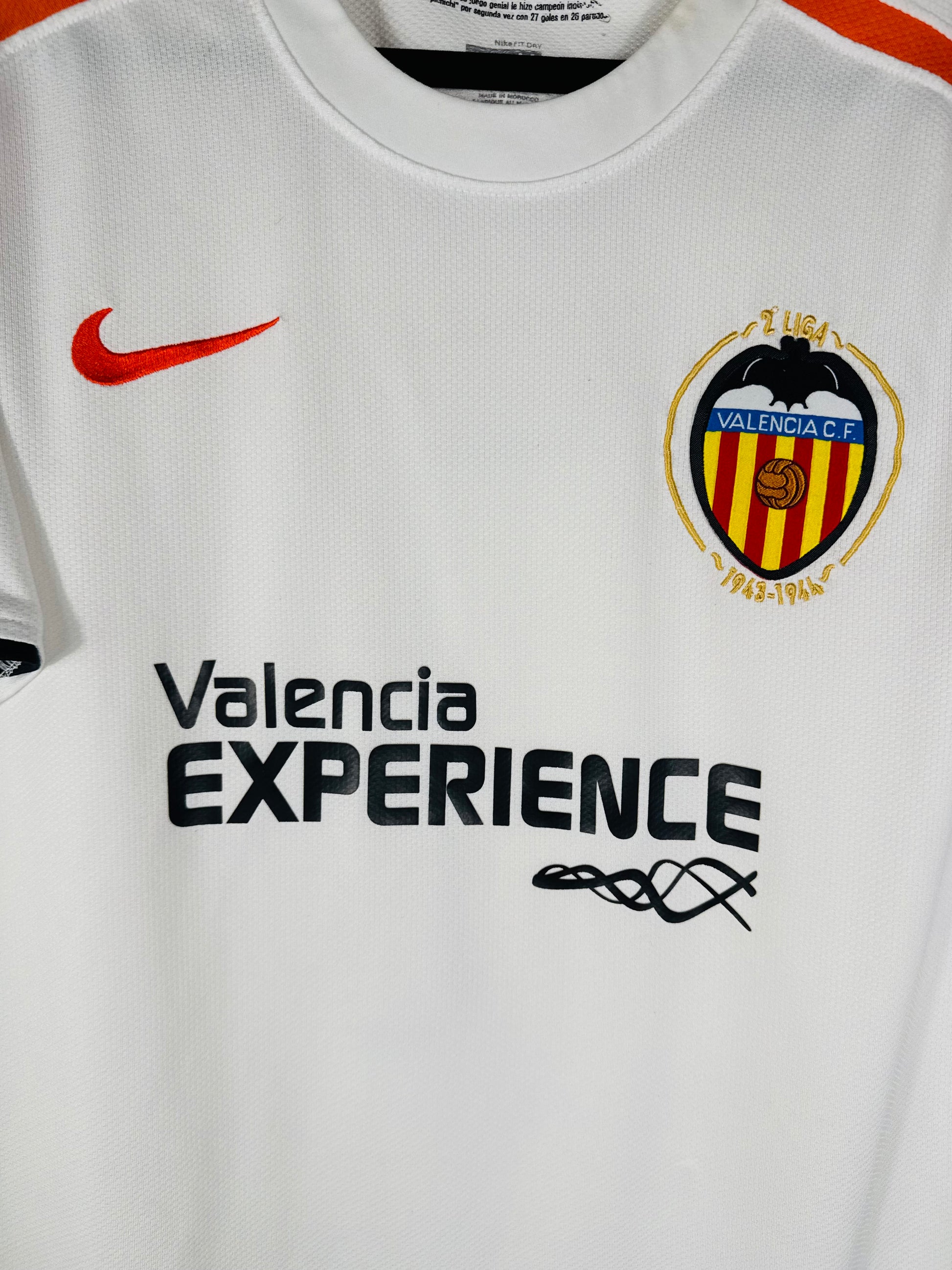 Gros plan sur l'écusson du Valencia CF et le sponsor "Valencia EXPERIENCE" sur le tissu blanc.