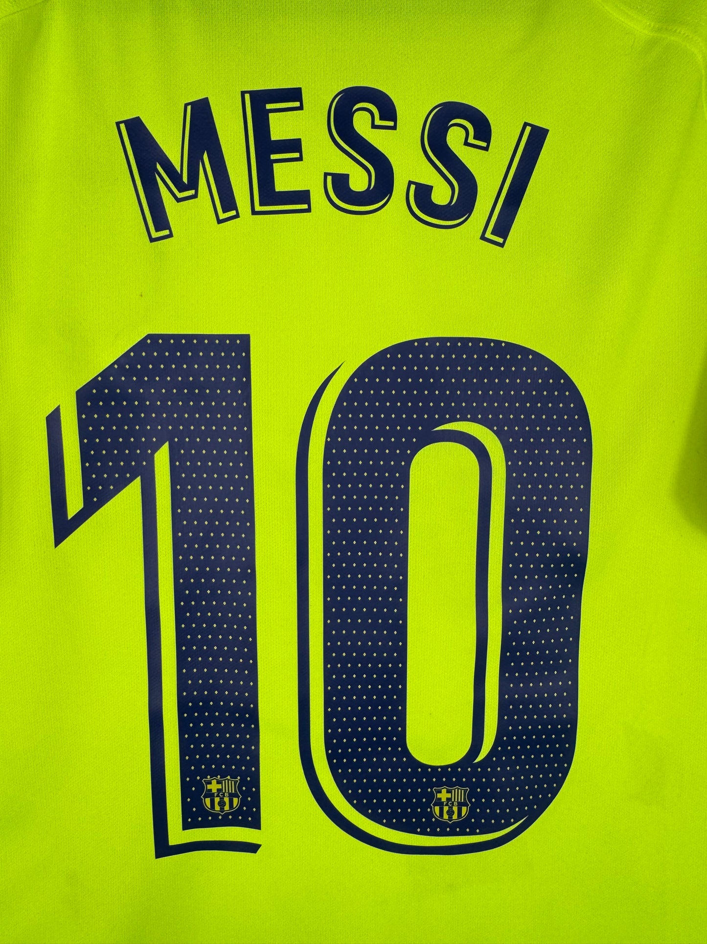Zoom sur le nom MESSI et le numéro 10 bleu marine, typographie officielle FC Barcelone.