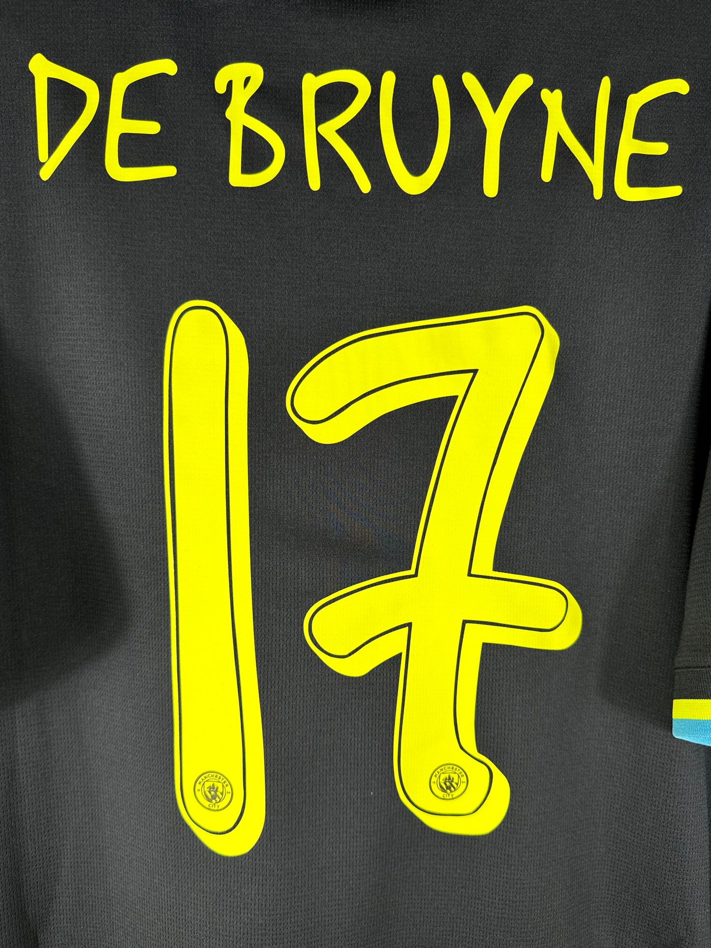 Zoom sur le numéro 17 et le lettrage jaune dessinés par Noel Gallagher, avec l'écusson du club intégré.