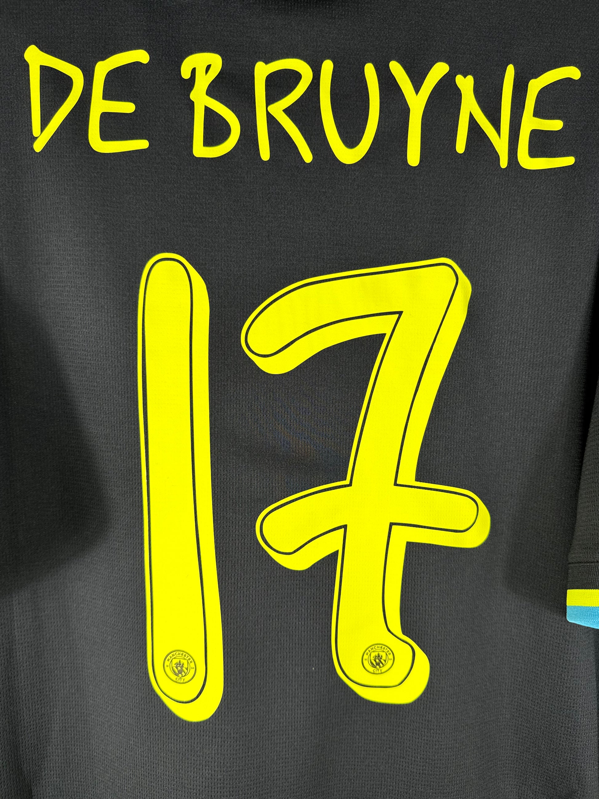 Zoom sur le numéro 17 et le lettrage jaune dessinés par Noel Gallagher, avec l'écusson du club intégré.