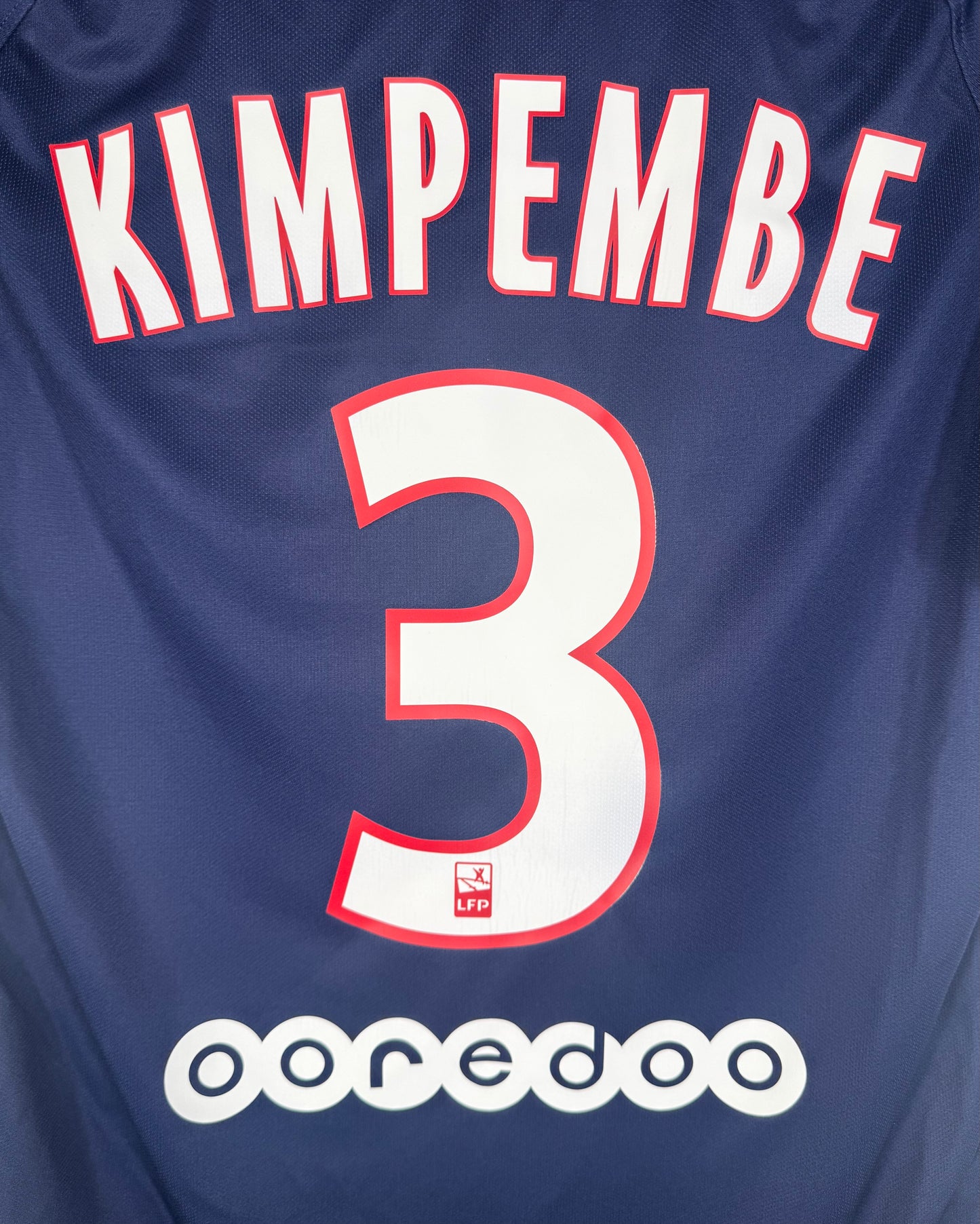 Zoom sur le nom KIMPEMBE et le numéro 3 blanc avec contour rouge.