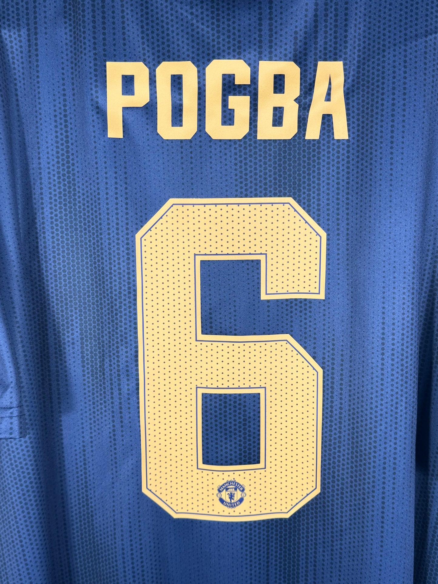 Zoom sur le nom POGBA et le numéro 6 blanc, police officielle Premier League.