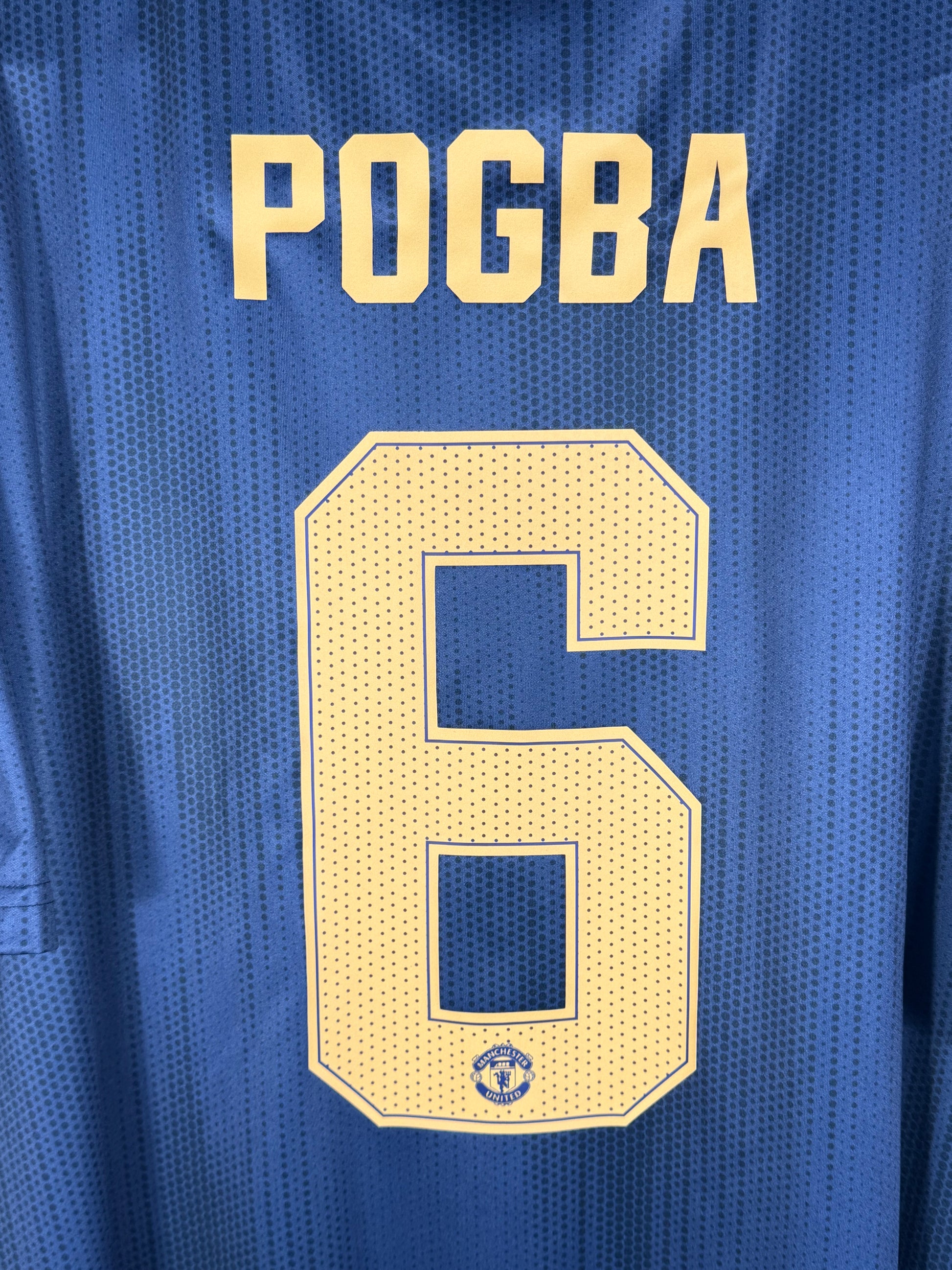 Zoom sur le nom POGBA et le numéro 6 blanc, police officielle Premier League.