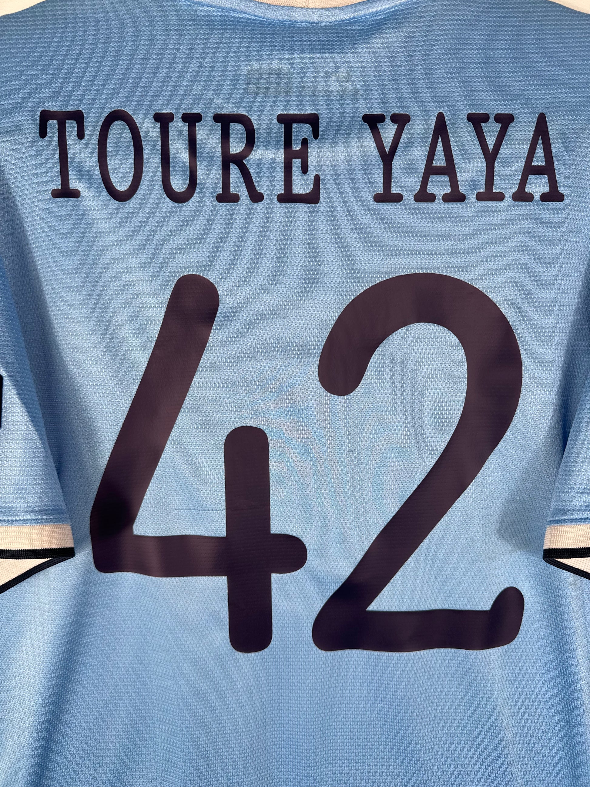 Zoom sur le nom TOURE YAYA et le numéro 42 bleu marine, typographie officielle européenne de Manchester City 2013-2014.