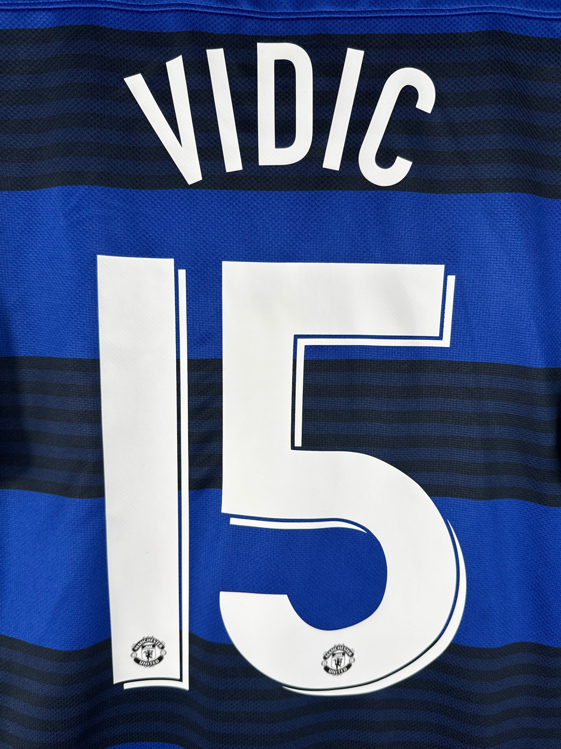 Zoom sur le nom VIDIC et le numéro 15 blanc avec le diable rouge intégré dans la base du chiffre, police Coupe d'Europe.