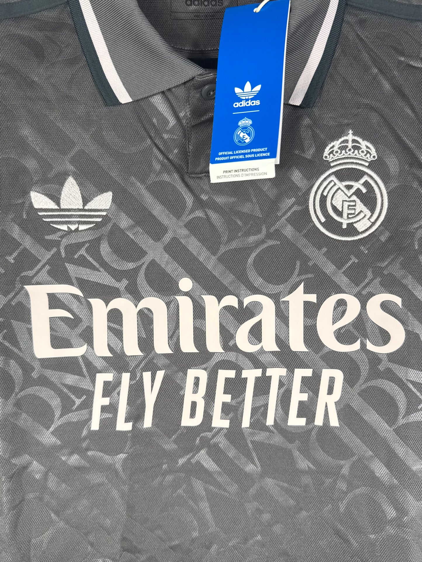Gros plan sur le logo vintage Adidas Trèfle et l'écusson Real Madrid sur fond gris texturé.