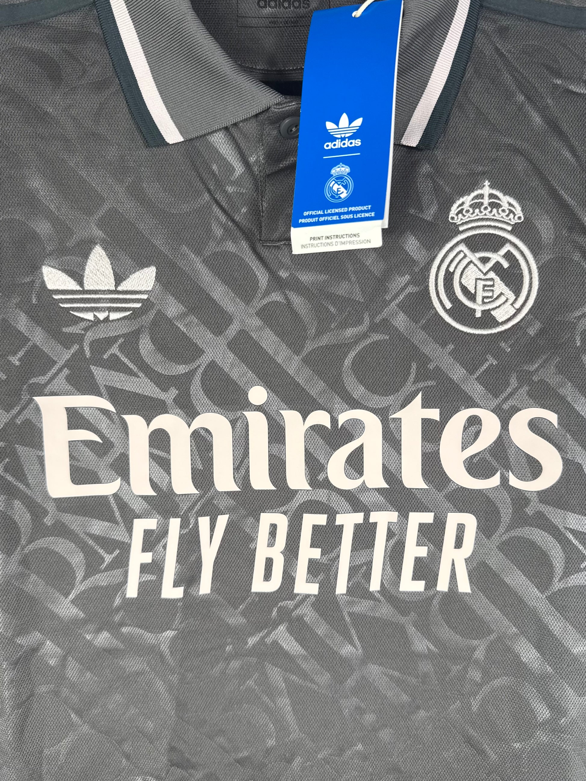 Gros plan sur le logo vintage Adidas Trèfle et l'écusson Real Madrid sur fond gris texturé.