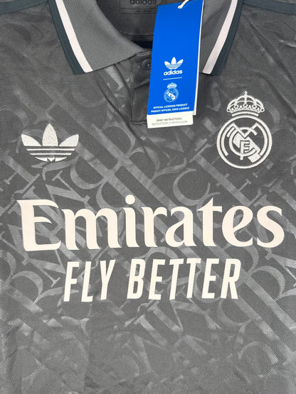 Gros plan sur le logo vintage Adidas Trèfle et l'écusson Real Madrid sur fond gris texturé.