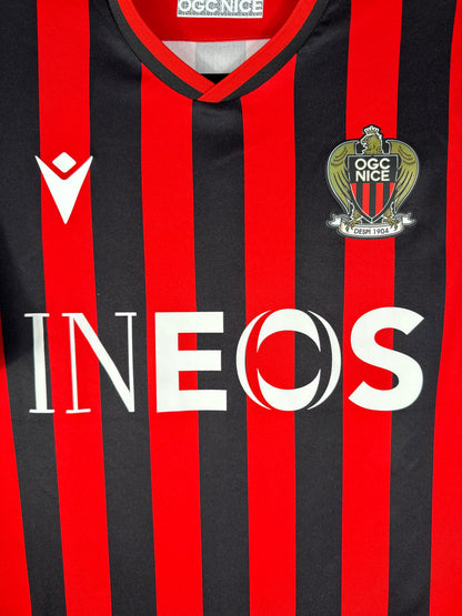 Gros plan sur l'écusson de l'OGC Nice, le logo Macron et le sponsor INEOS sur le torse.