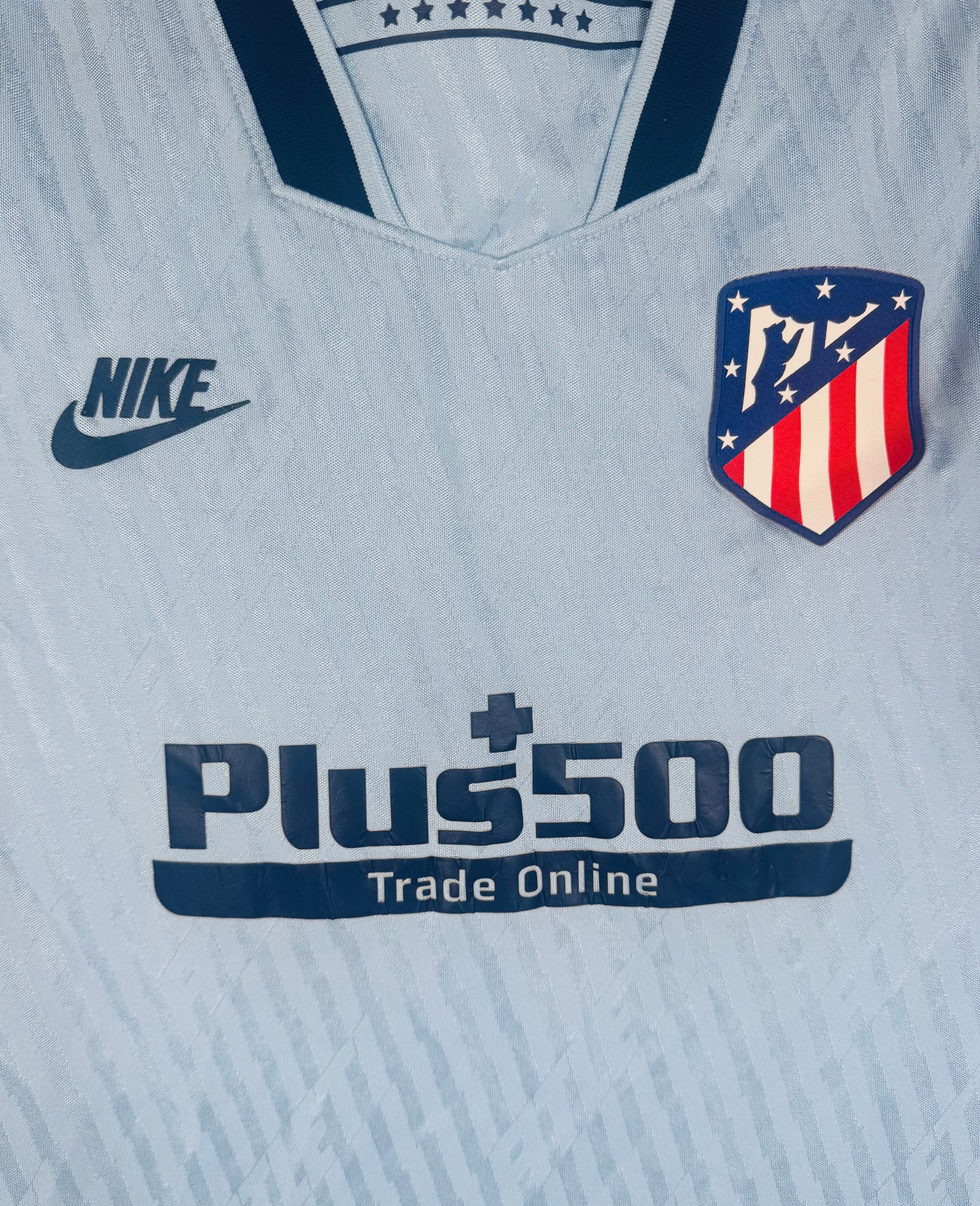Gros plan sur le logo Nike Futura vintage et l'écusson Atletico sur fond bleu.
