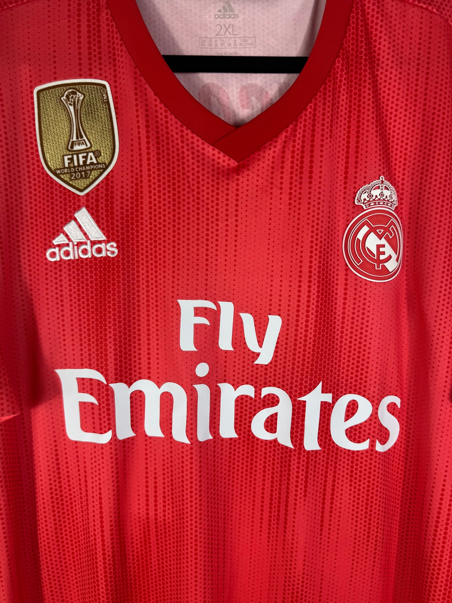 Gros plan sur l'écusson monochrome du Real Madrid, le badge FIFA doré et le logo Adidas blanc.