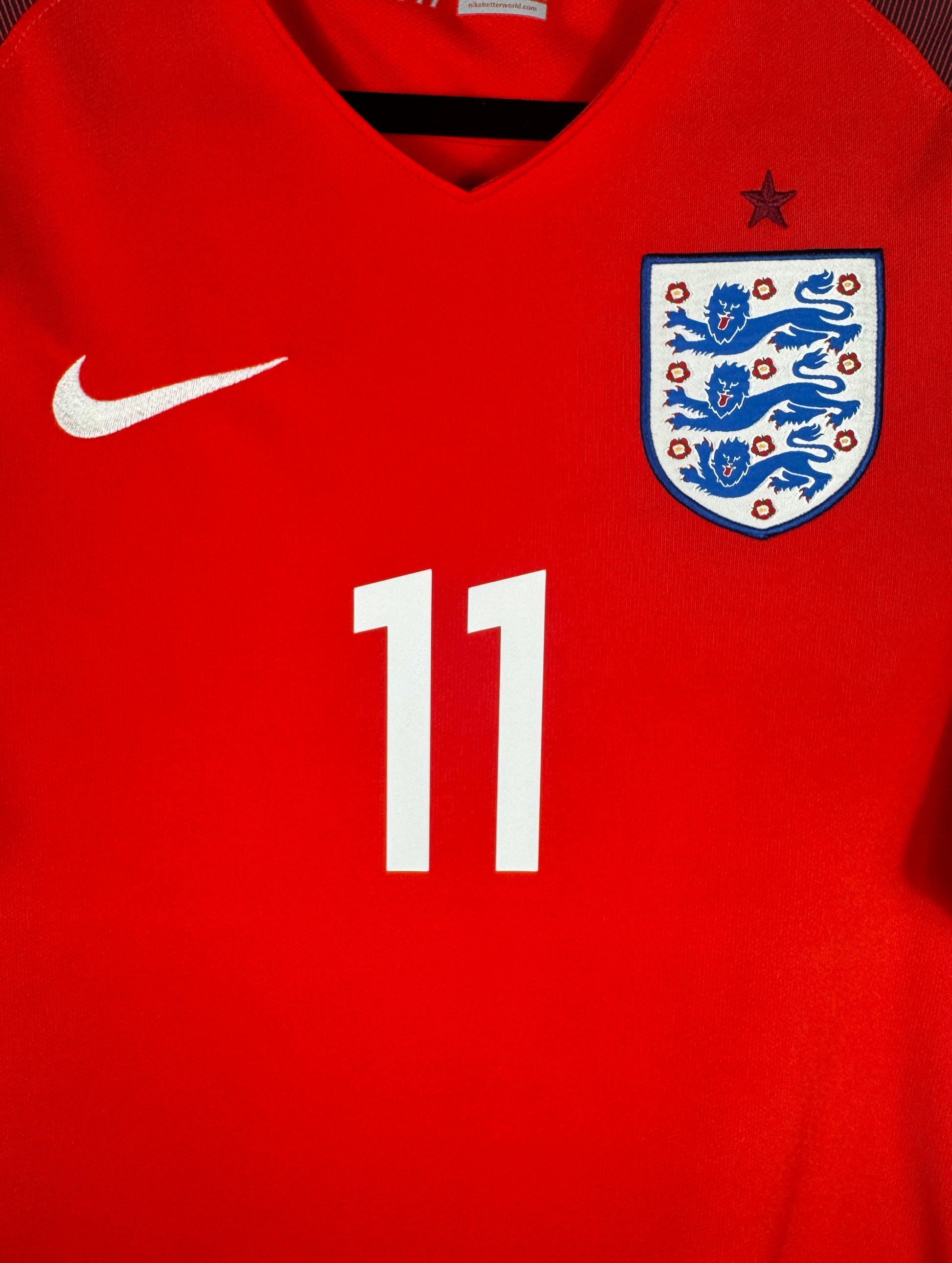 Gros plan sur le numéro 11 blanc et l'écusson des Three Lions sur fond rouge.