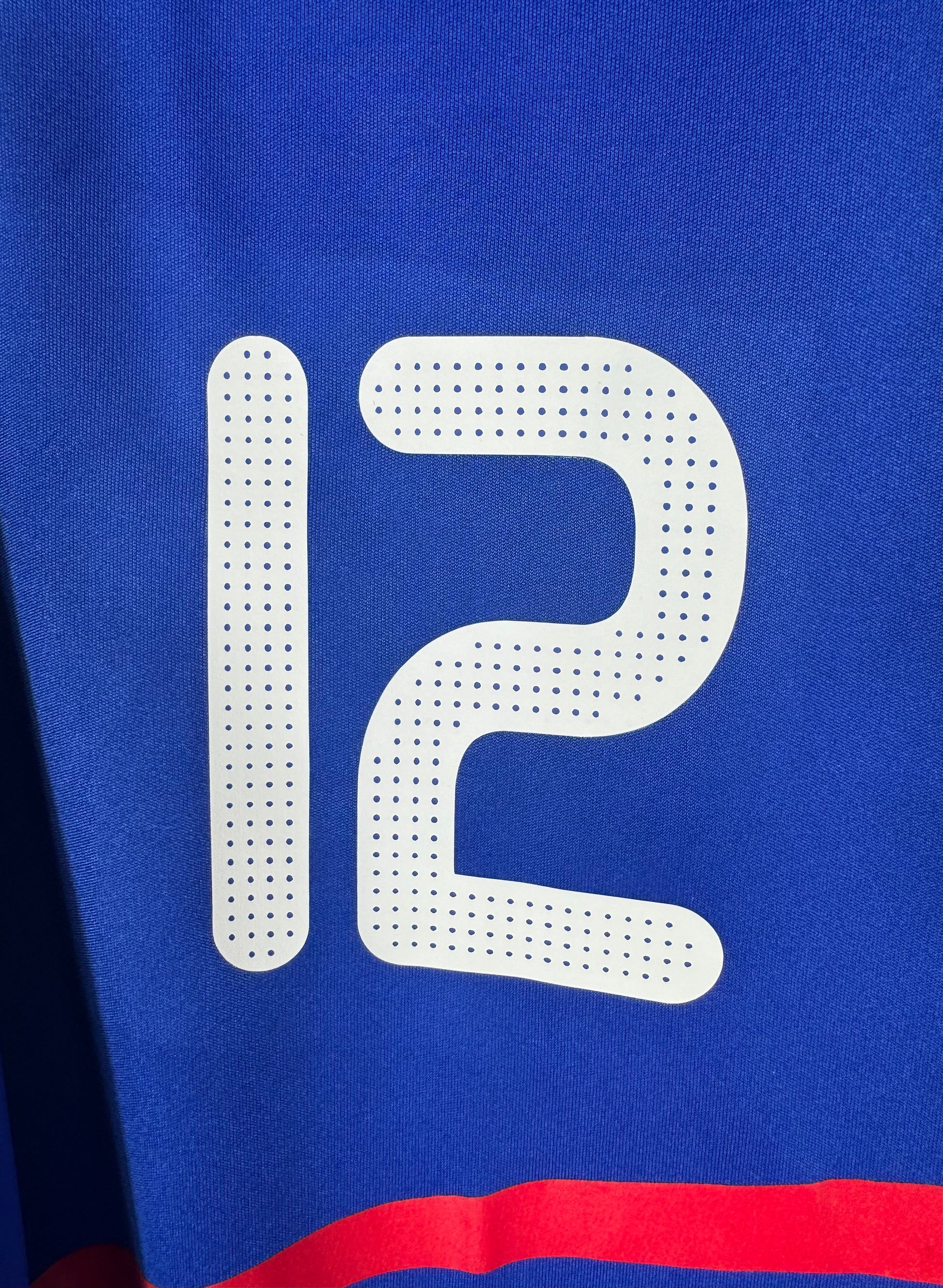 Gros plan sur le numéro 12 perforé floqué sur la poitrine du maillot bleu.