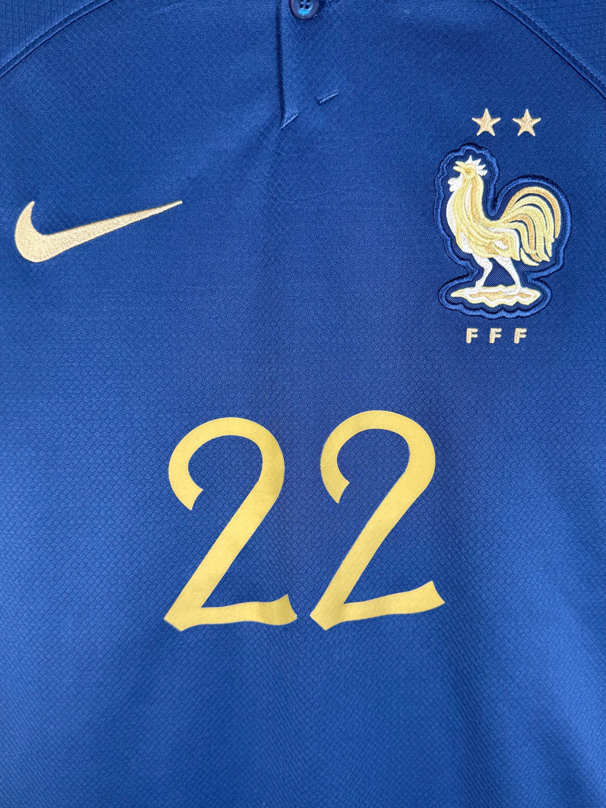 Détail écusson FFF deux étoiles et numéro 22 doré sur maillot France.