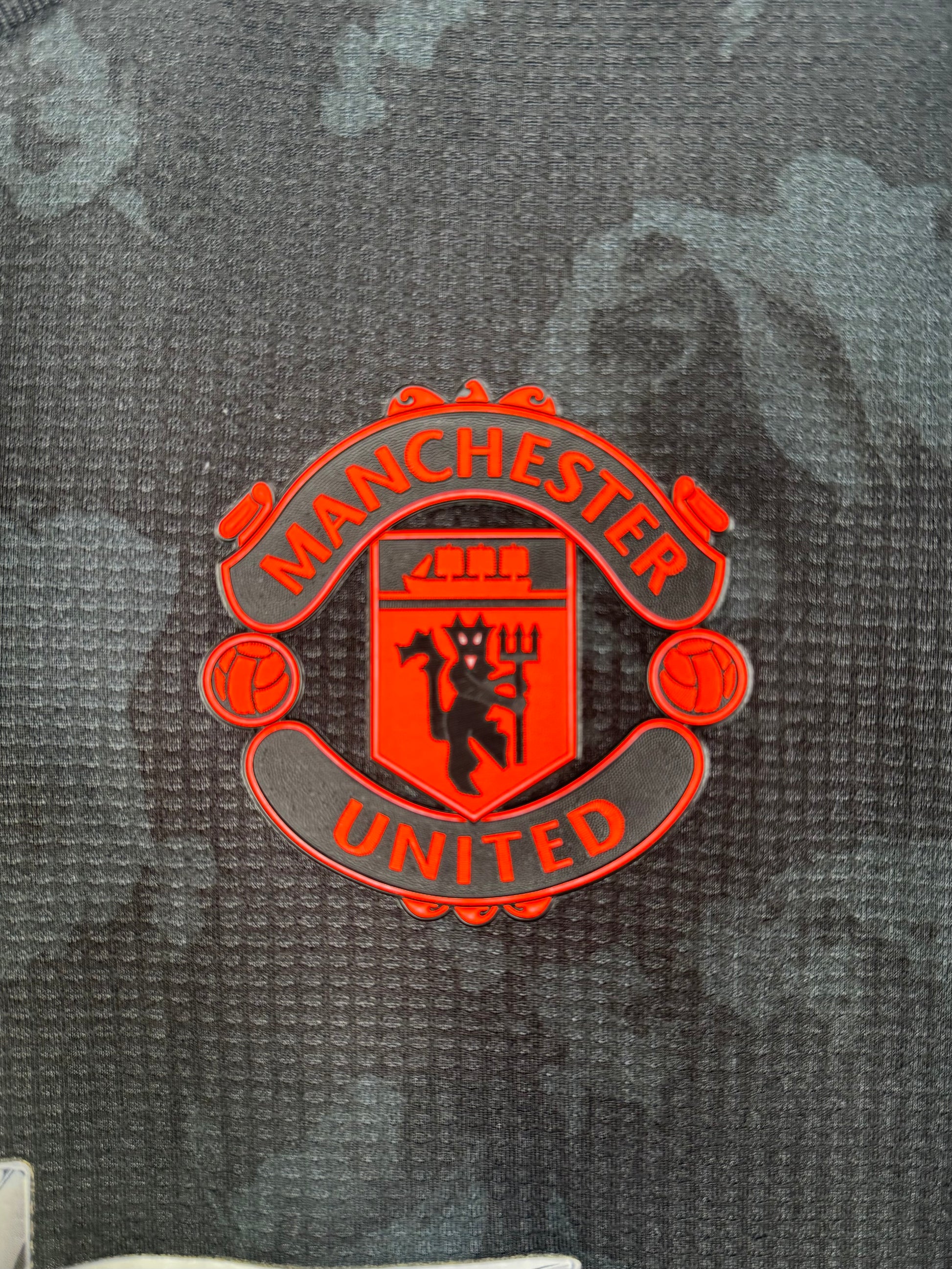 Détail écusson Manchester United thermocollé (version pro) sur maillot third noir.