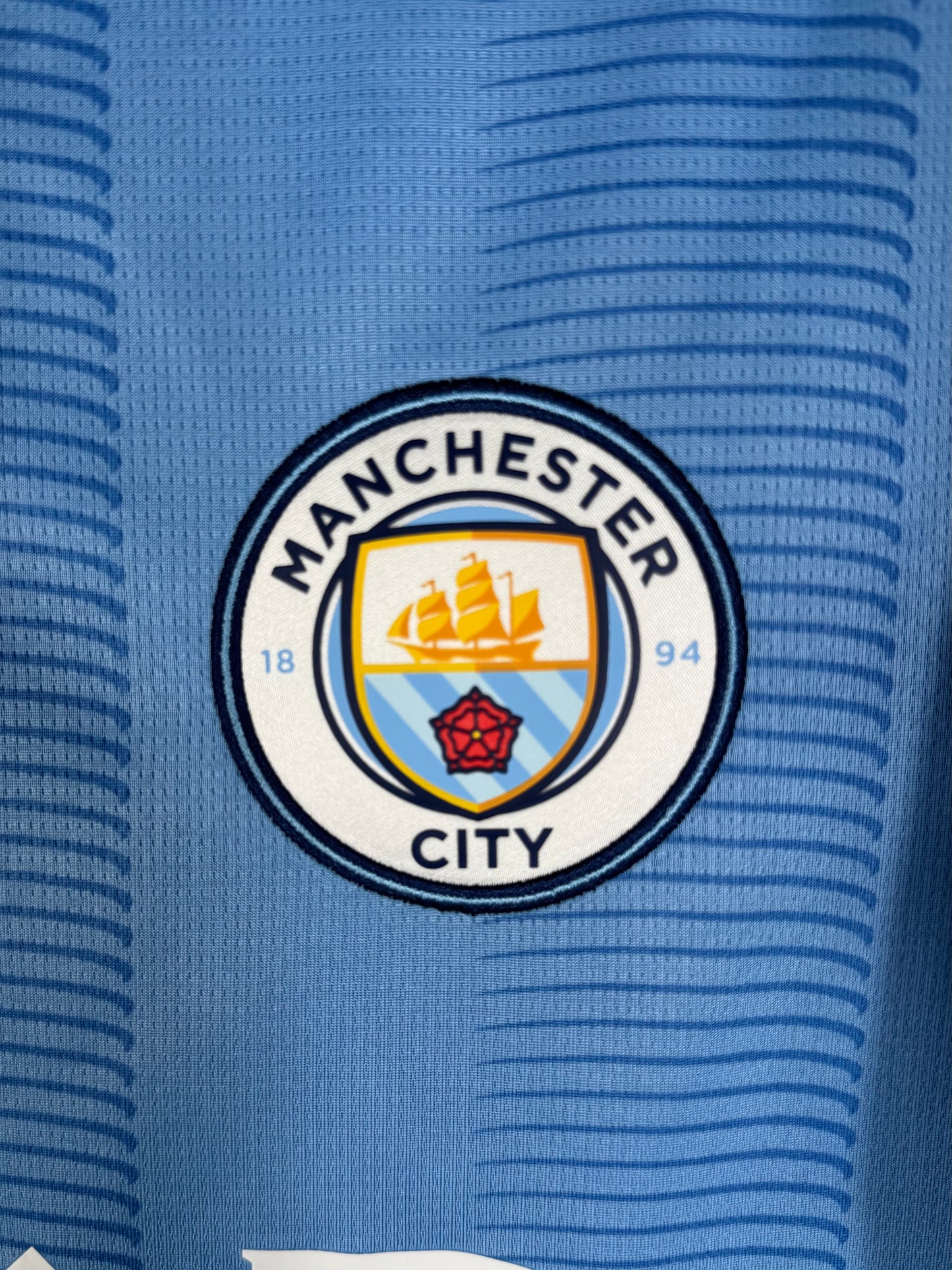 Détail écusson Manchester City brodé sur maillot domicile Puma.
