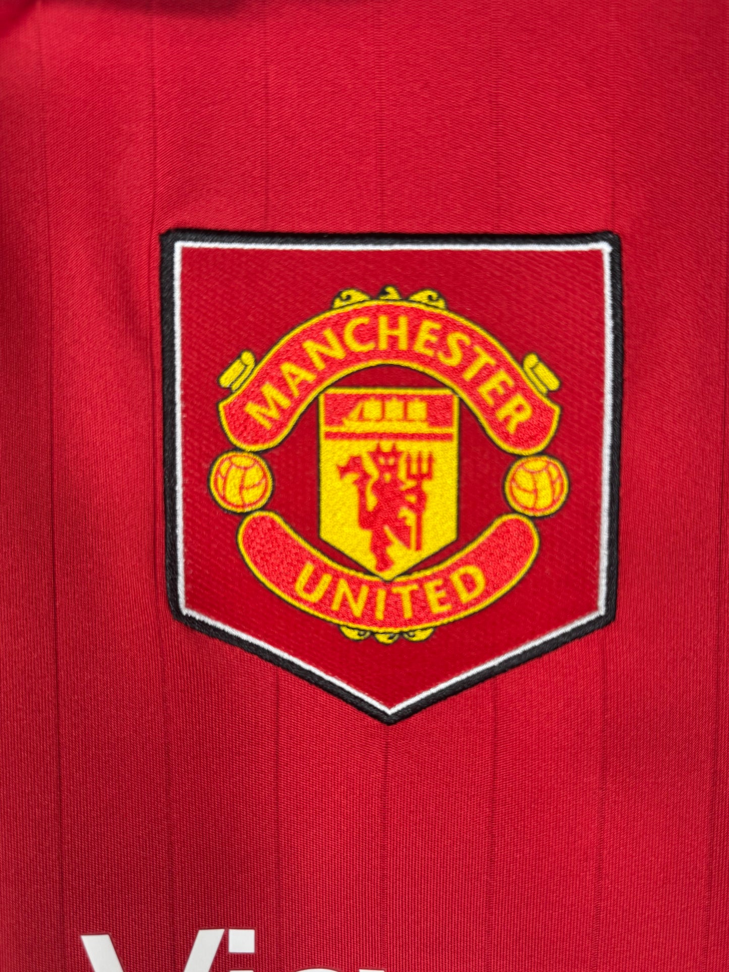 Détail écusson Manchester United avec bouclier rétro sur maillot domicile.