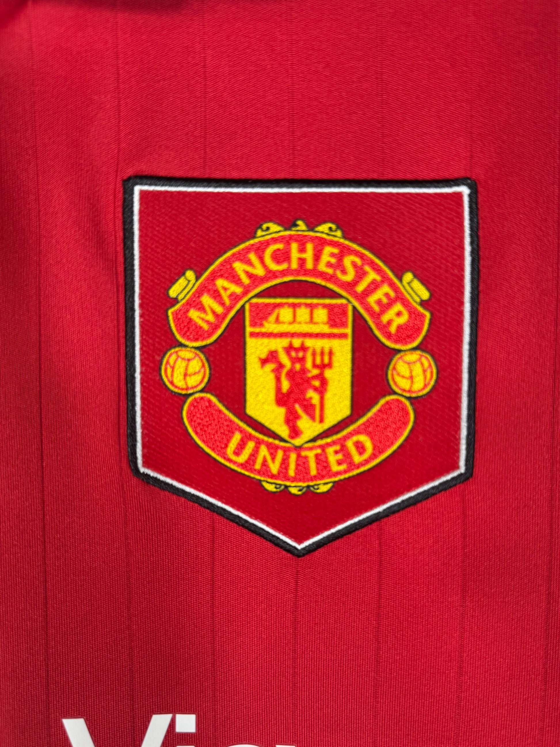 Détail écusson Manchester United avec bouclier rétro sur maillot domicile.
