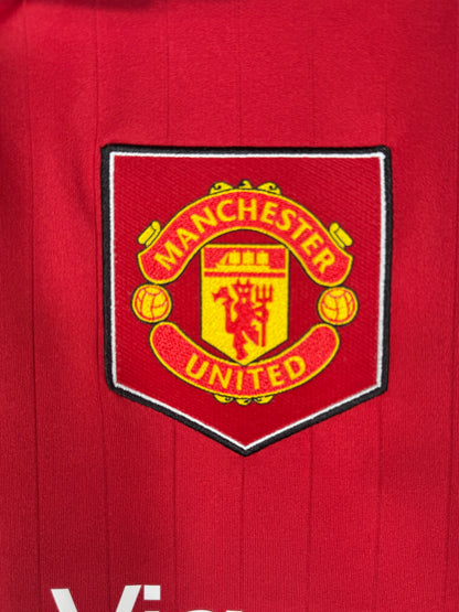 Détail écusson Manchester United avec bouclier rétro sur maillot domicile.