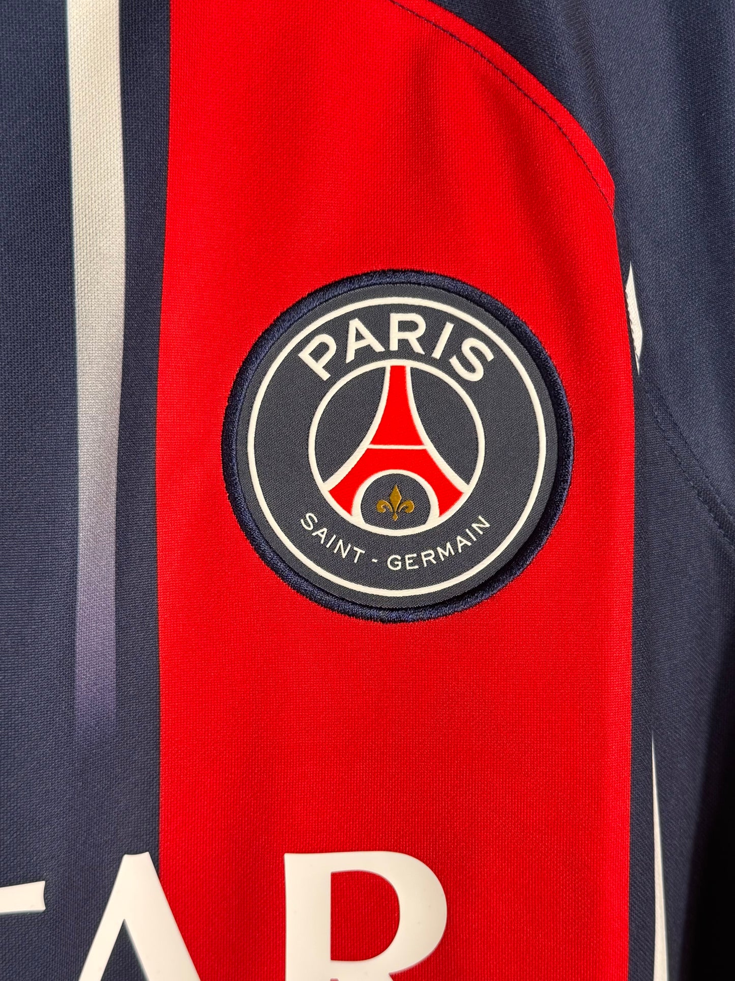 Détail écusson Paris Saint-Germain et texture bande rouge fondue maillot domicile.